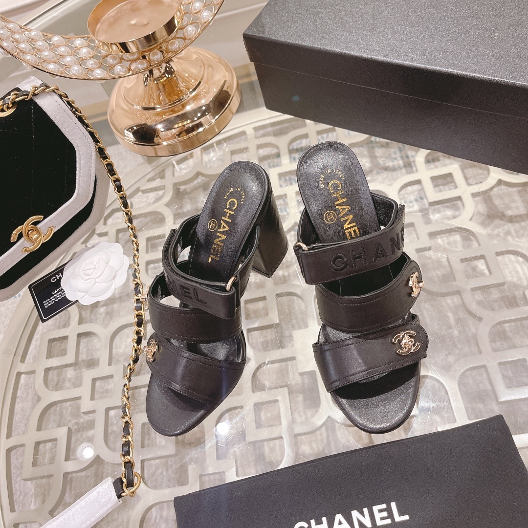 A pair of luxury Chanel black leather triple strap block heel mules with gold CC logos displayed on a glass table - Hình 2