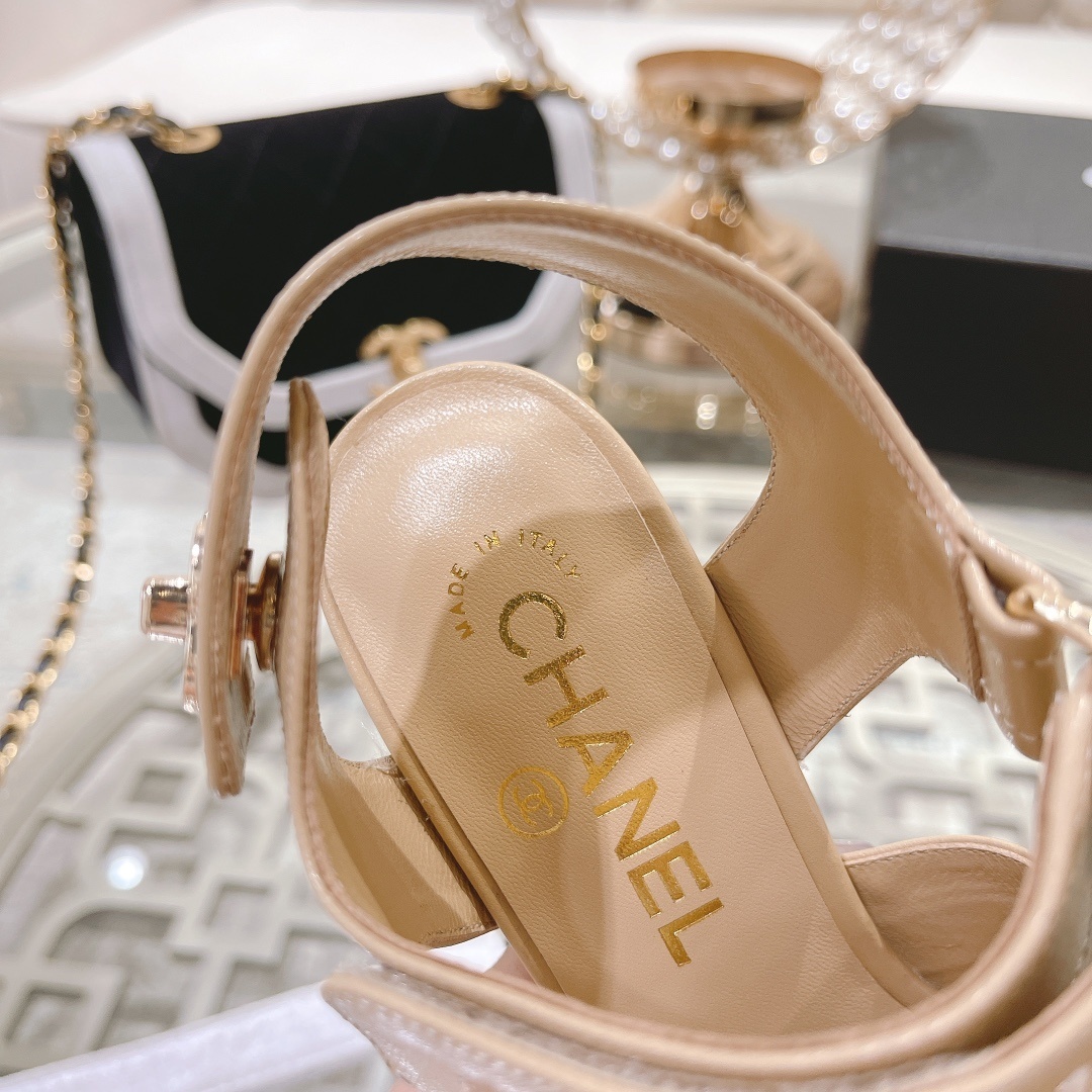 Pair of Chanel beige leather block heel sandals with gold CC logo hardware and branded ankle straps displayed on a glass table. - Hình 9