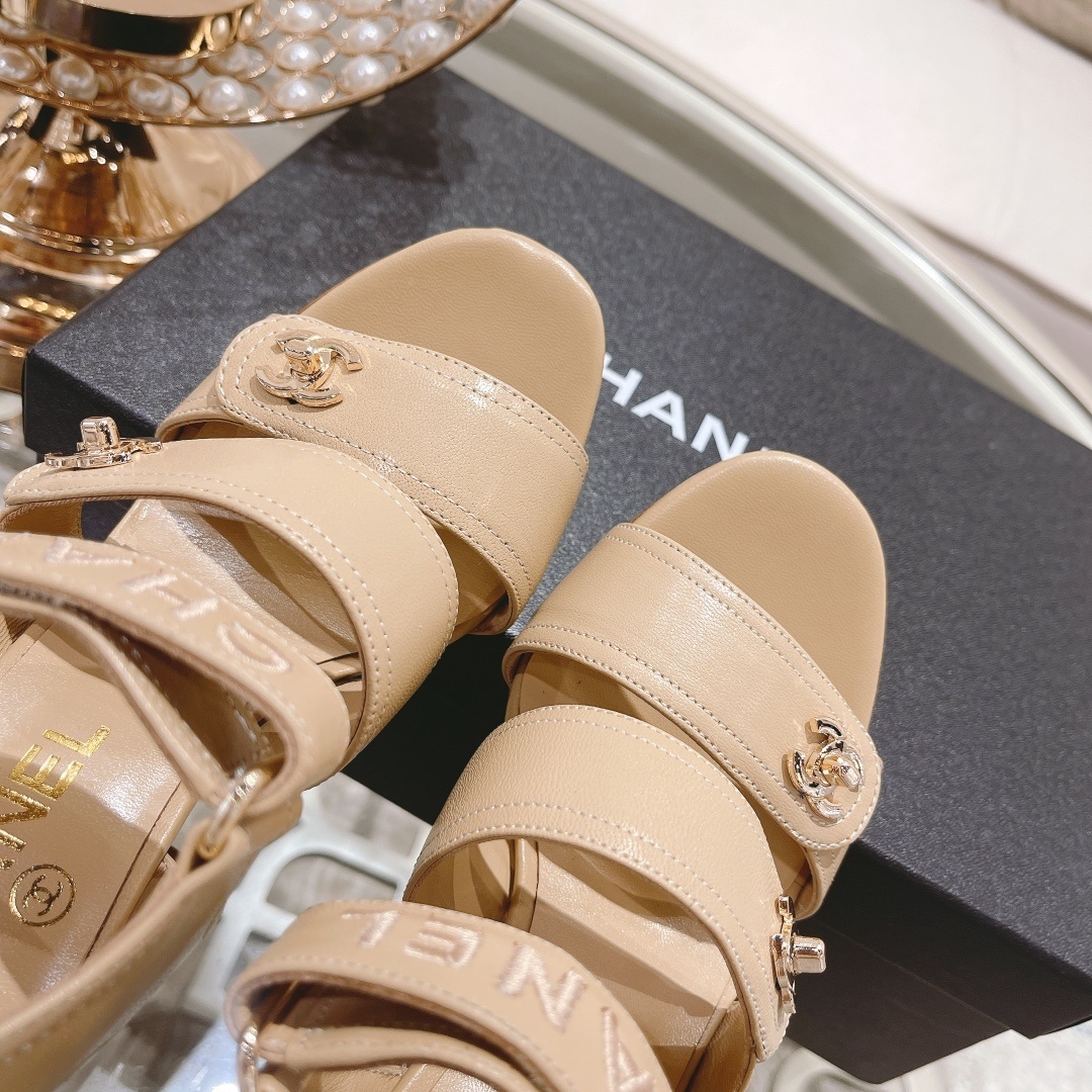Pair of Chanel beige leather block heel sandals with gold CC logo hardware and branded ankle straps displayed on a glass table. - Hình 8
