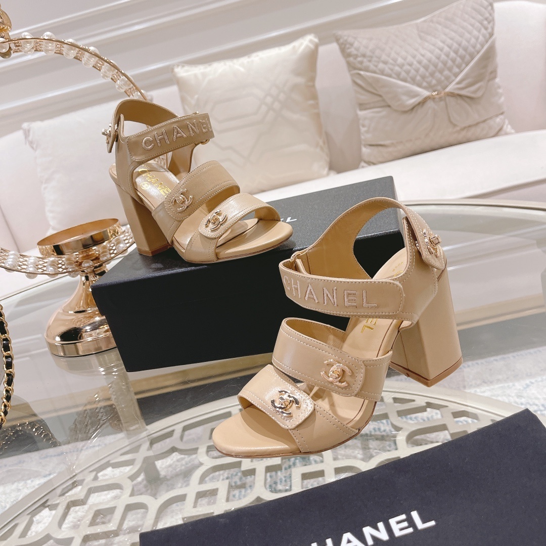 Pair of Chanel beige leather block heel sandals with gold CC logo hardware and branded ankle straps displayed on a glass table. - Hình 6