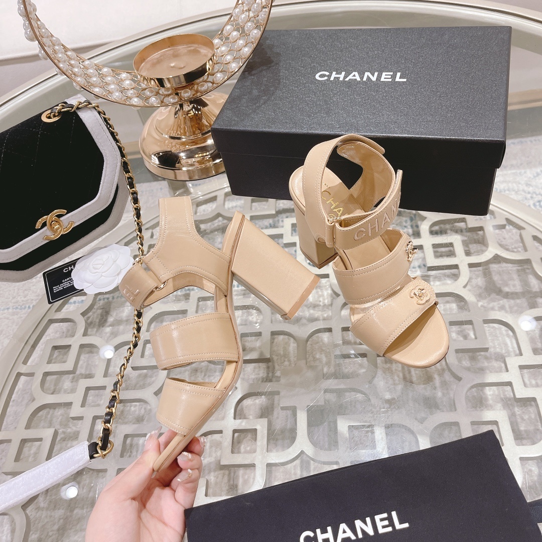 Pair of Chanel beige leather block heel sandals with gold CC logo hardware and branded ankle straps displayed on a glass table. - Hình 4