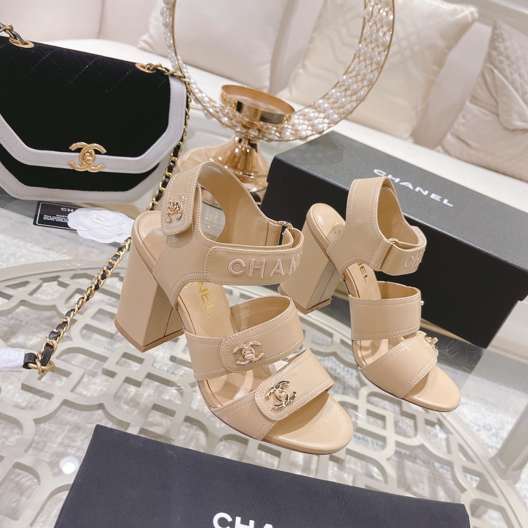Pair of Chanel beige leather block heel sandals with gold CC logo hardware and branded ankle straps displayed on a glass table. - Hình 3