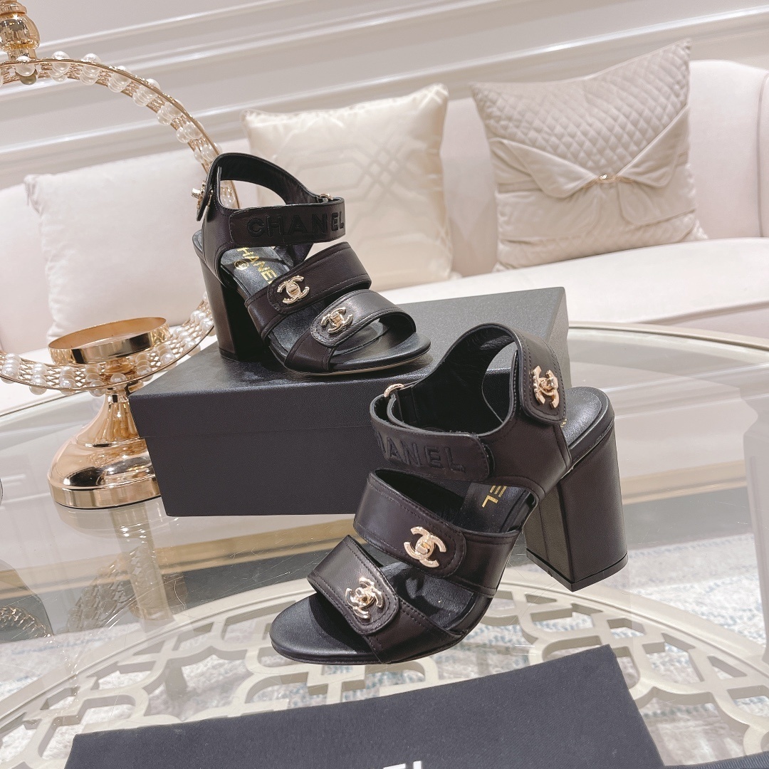 Pair of luxury black Chanel block heel sandals with gold CC logos and triple straps on a glass table - Hình 6