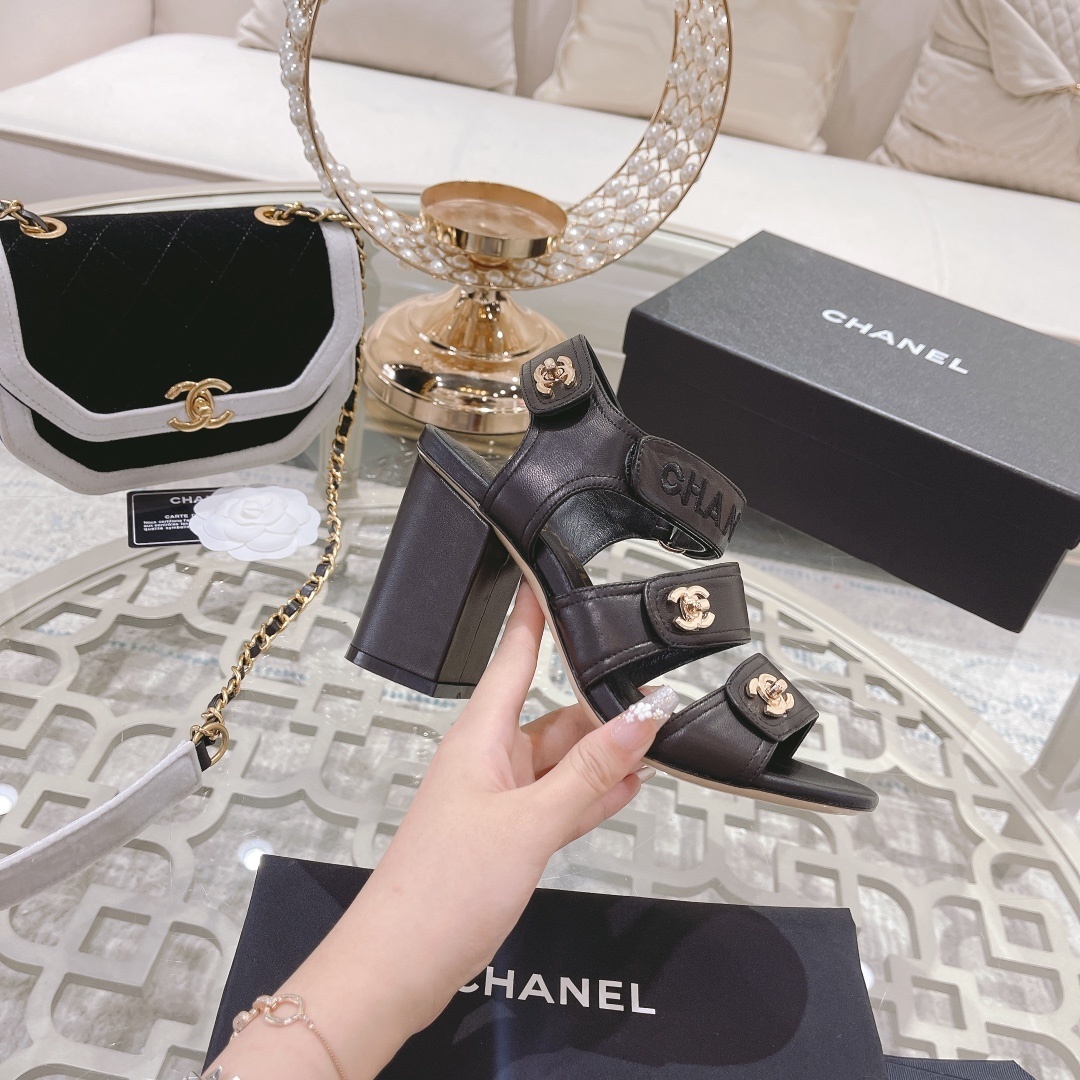 Pair of luxury black Chanel block heel sandals with gold CC logos and triple straps on a glass table - Hình 5
