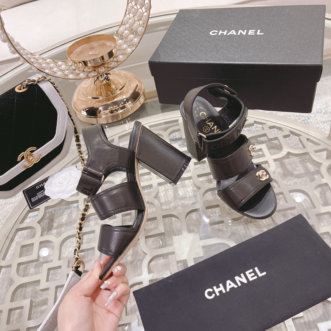 Pair of luxury black Chanel block heel sandals with gold CC logos and triple straps on a glass table - Hình 4