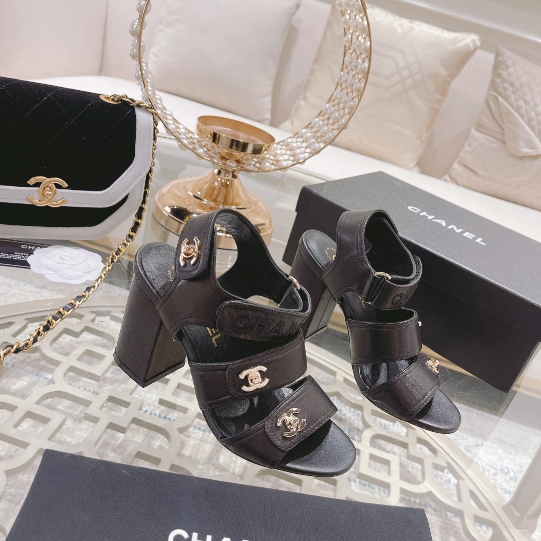 Pair of luxury black Chanel block heel sandals with gold CC logos and triple straps on a glass table - Hình 3