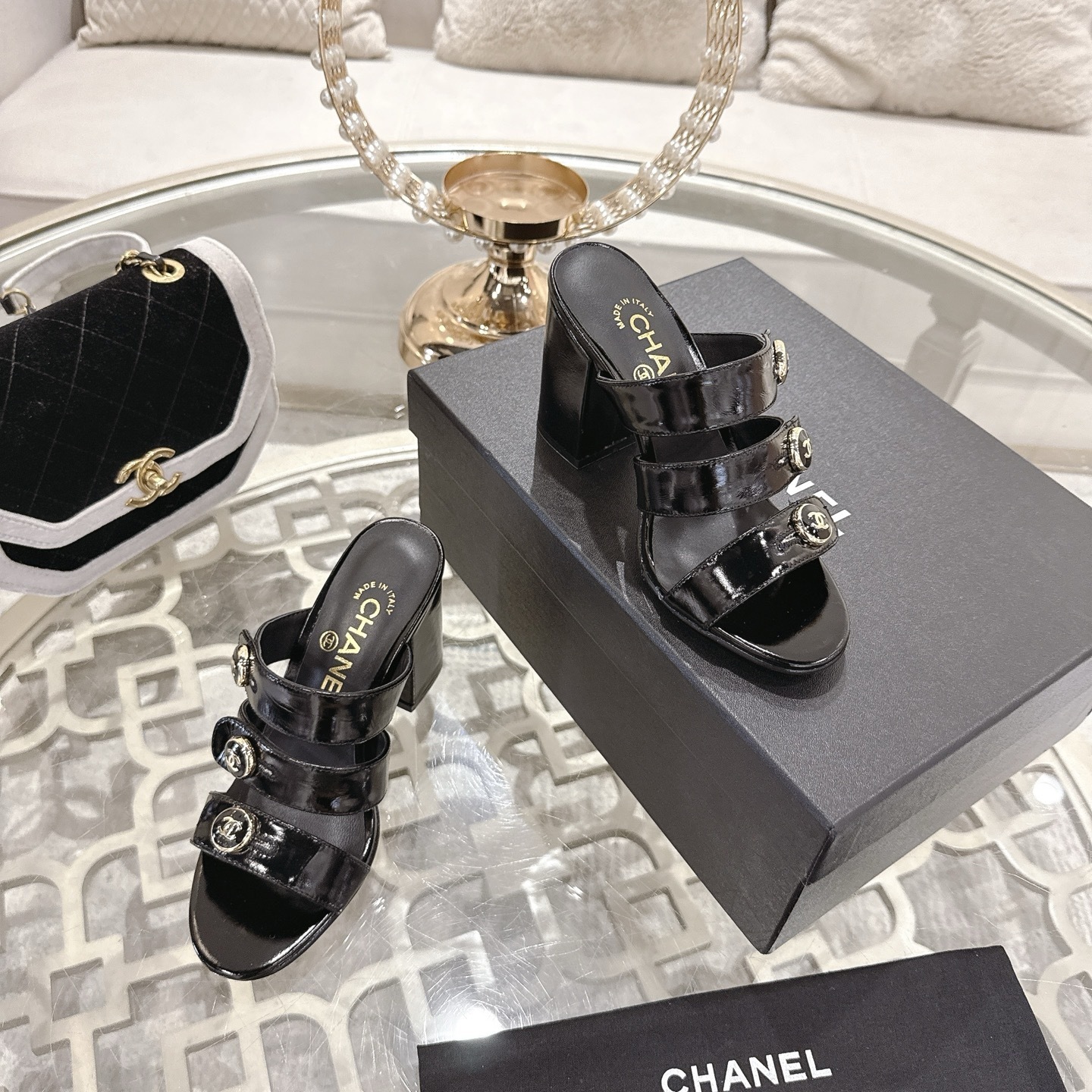 Luxury black patent leather sandals with triple straps and gold CC logo buttons on a designer glass table background. - Hình 6