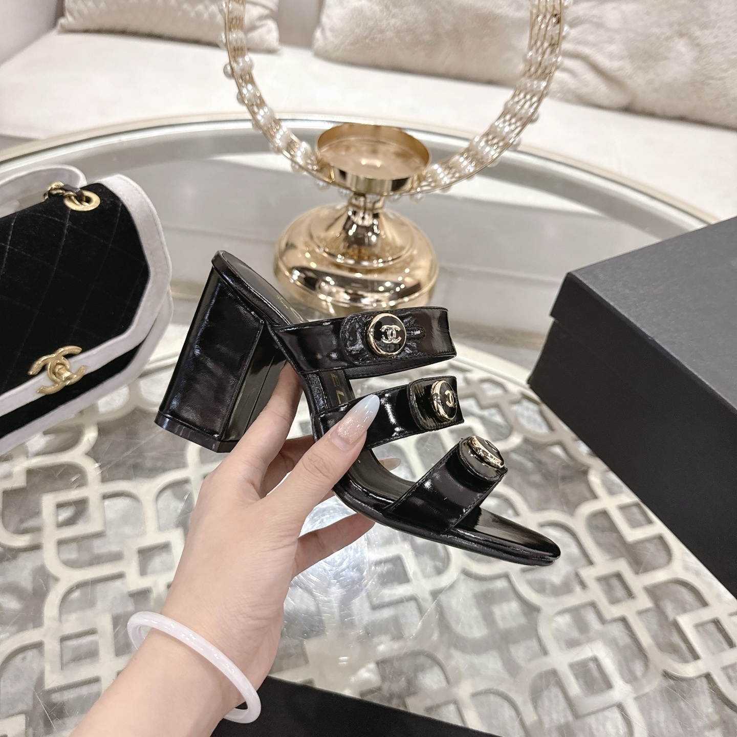 Luxury black patent leather sandals with triple straps and gold CC logo buttons on a designer glass table background. - Hình 5