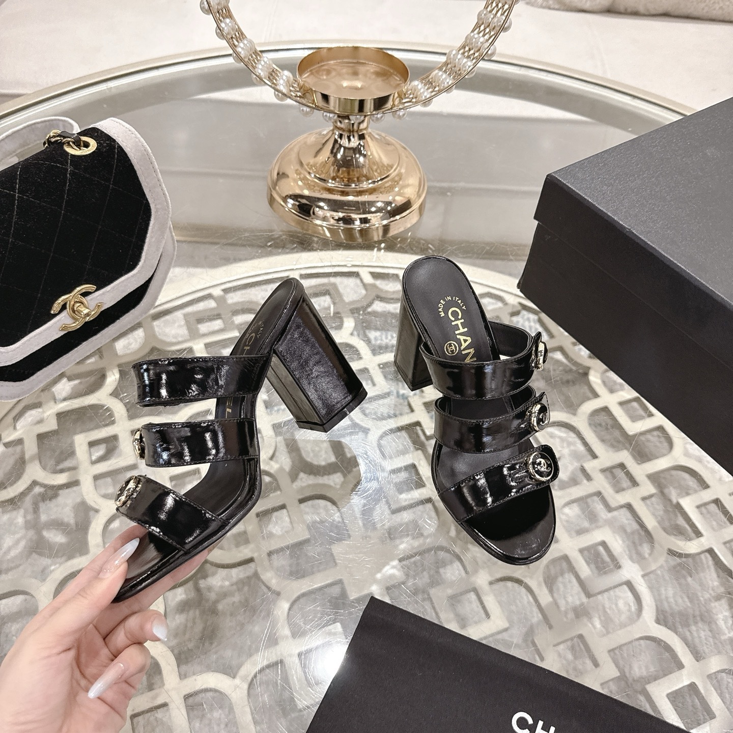 Luxury black patent leather sandals with triple straps and gold CC logo buttons on a designer glass table background. - Hình 4