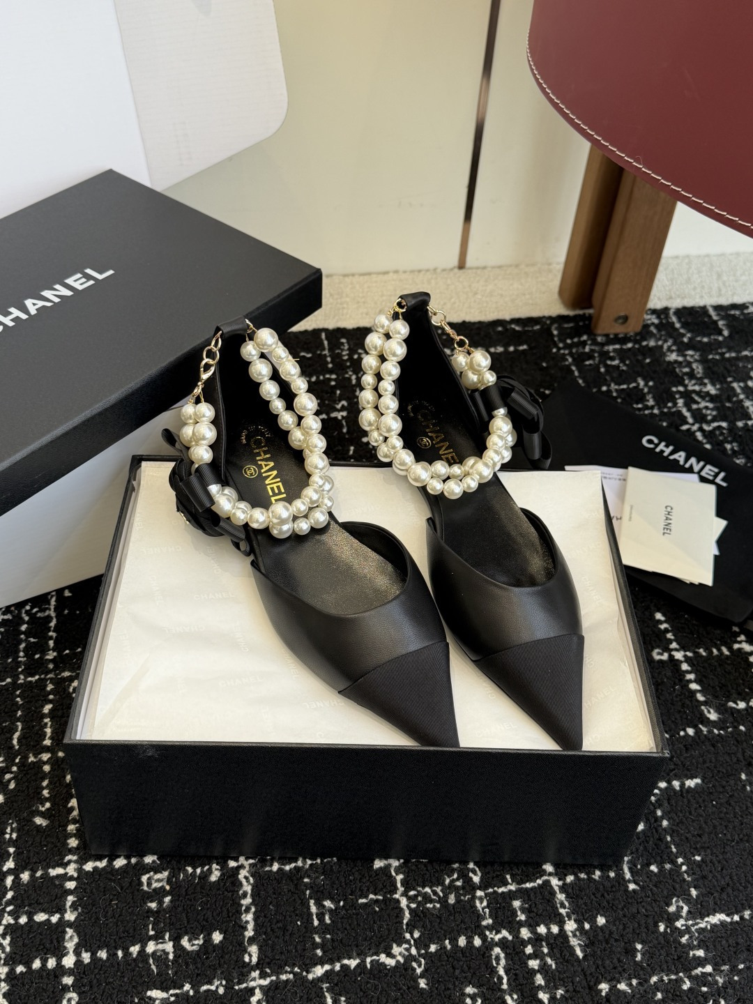 Pair of black Chanel leather pointed-toe flats featuring double pearl ankle straps and black camellia flower details with gold CC logo. - Hình 4