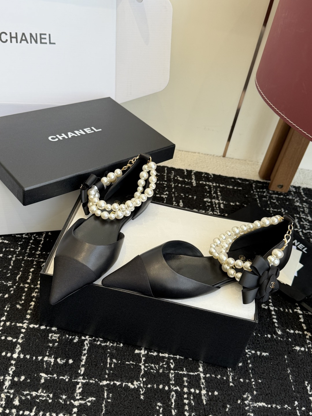 Pair of black Chanel leather pointed-toe flats featuring double pearl ankle straps and black camellia flower details with gold CC logo. - Hình 3