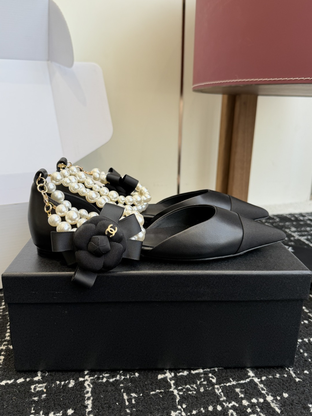 Pair of black Chanel leather pointed-toe flats featuring double pearl ankle straps and black camellia flower details with gold CC logo. - Hình 2
