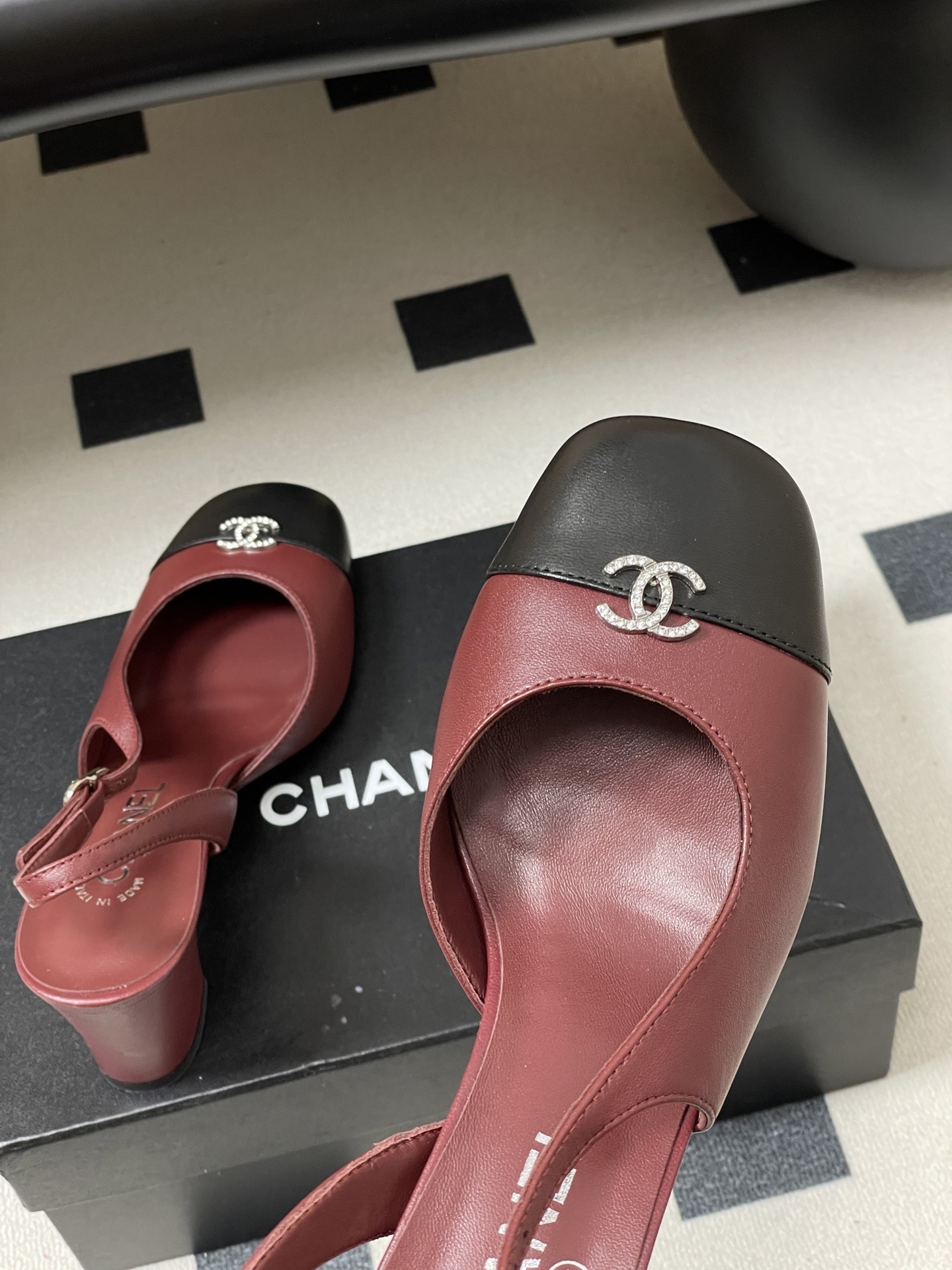A pair of Chanel burgundy leather slingback heels with black cap toes and crystal-embellished CC logos on a black surface. - Hình 9
