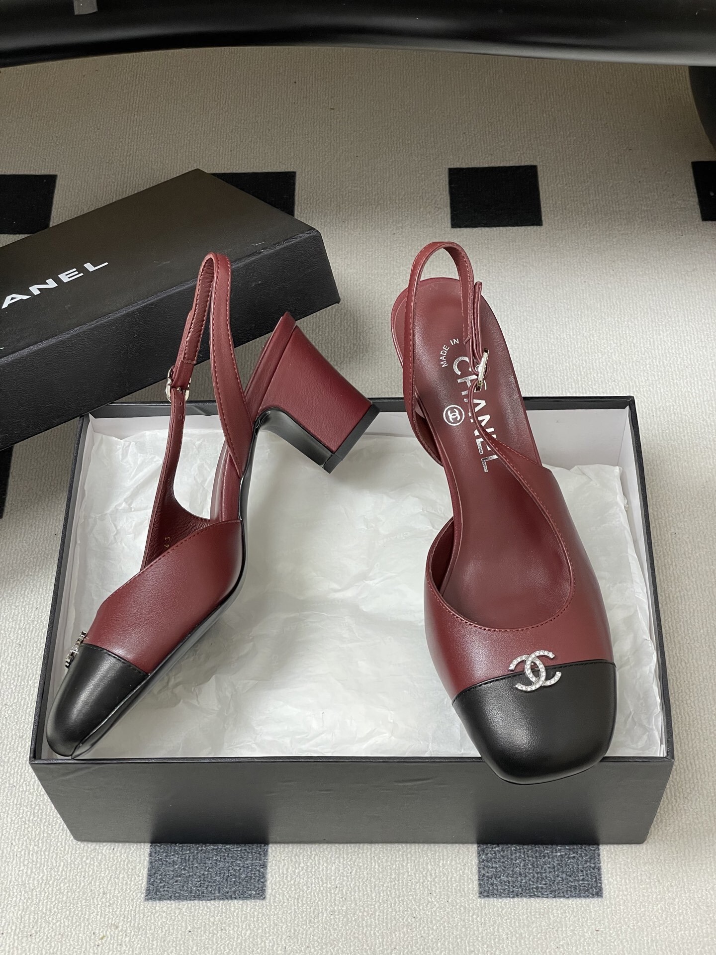 A pair of Chanel burgundy leather slingback heels with black cap toes and crystal-embellished CC logos on a black surface. - Hình 6