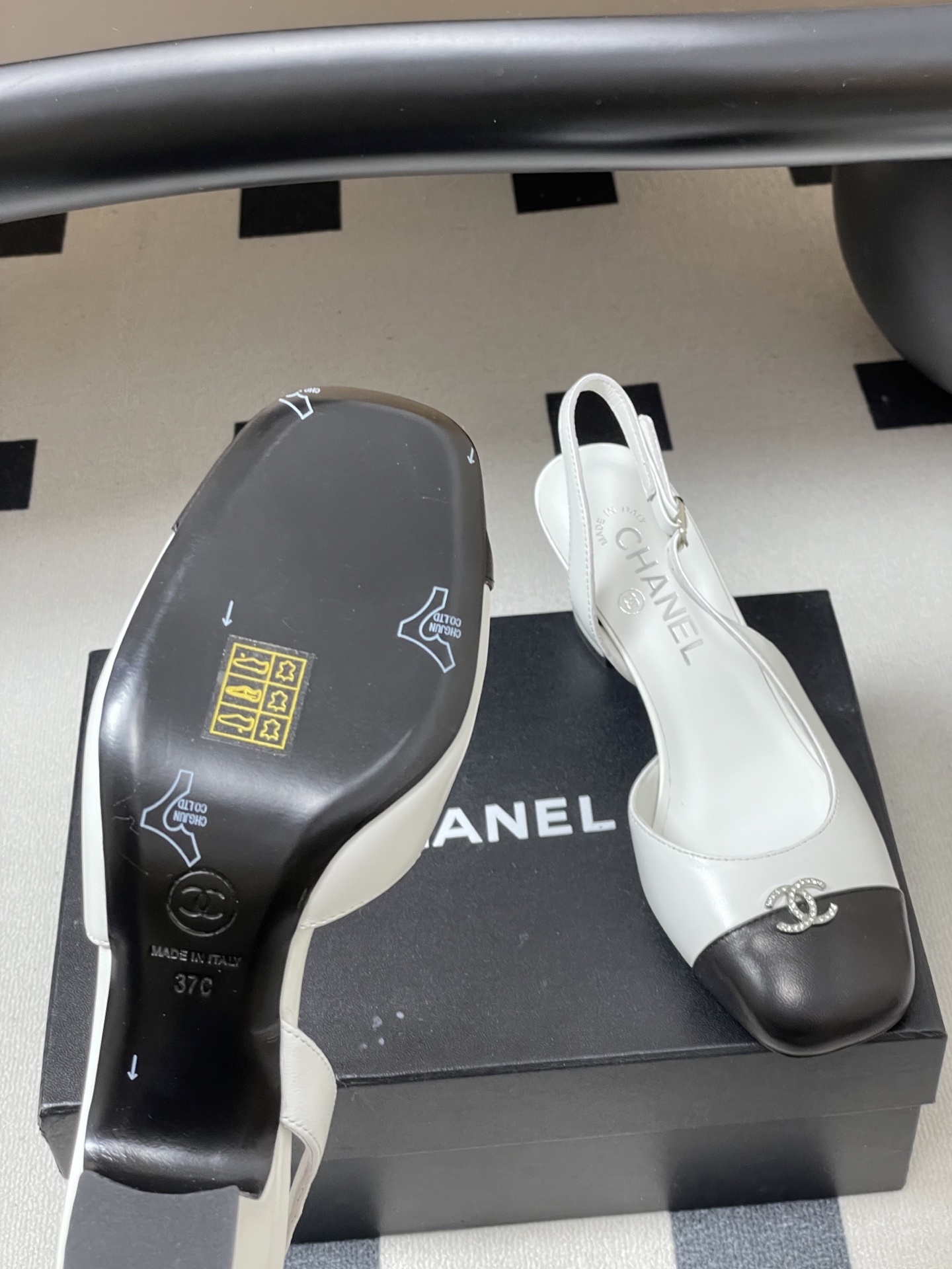 Pair of Chanel white leather slingback pumps with black toe caps and crystal CC logos on a black table. - Hình 8