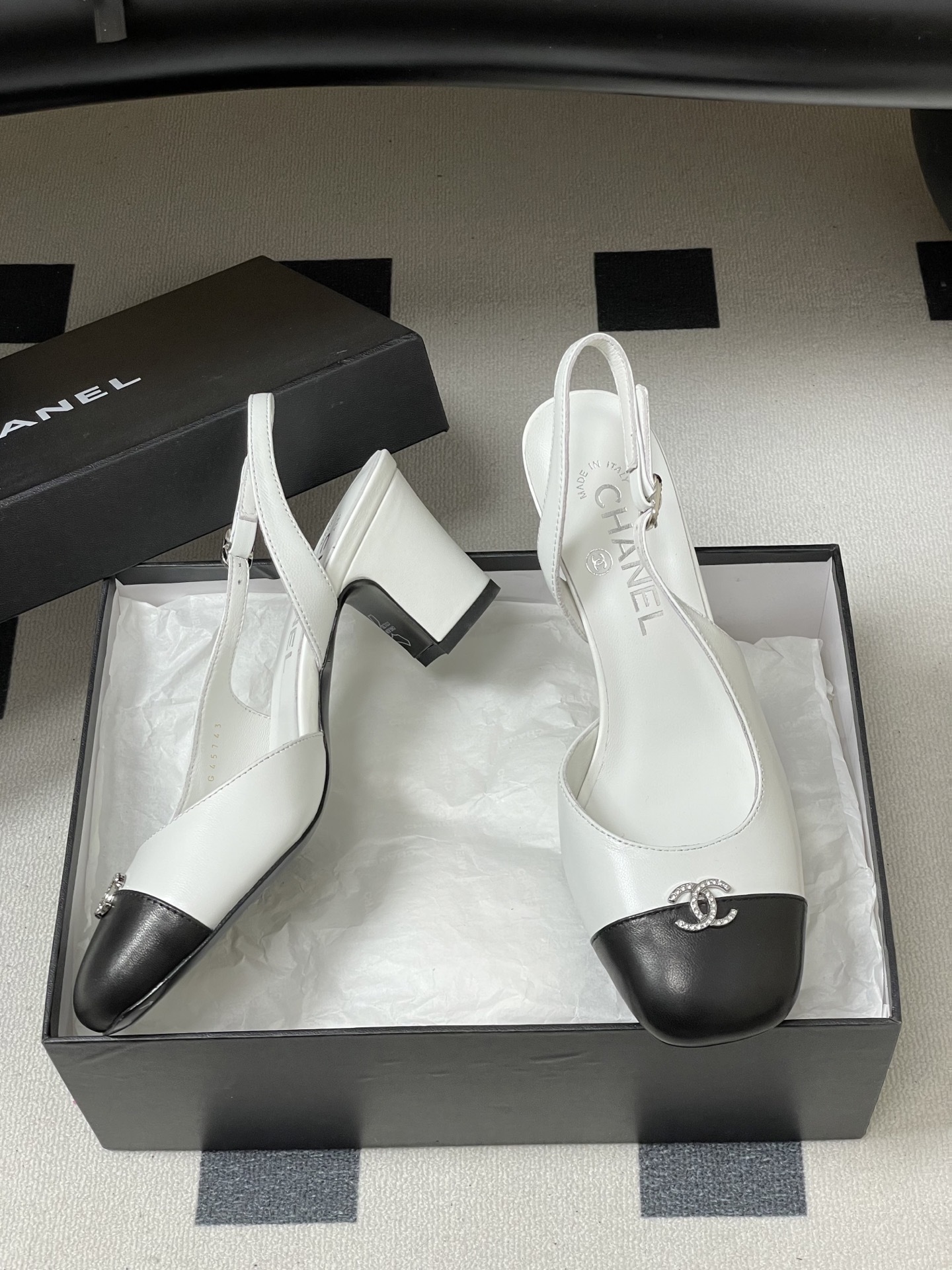 Pair of Chanel white leather slingback pumps with black toe caps and crystal CC logos on a black table. - Hình 6