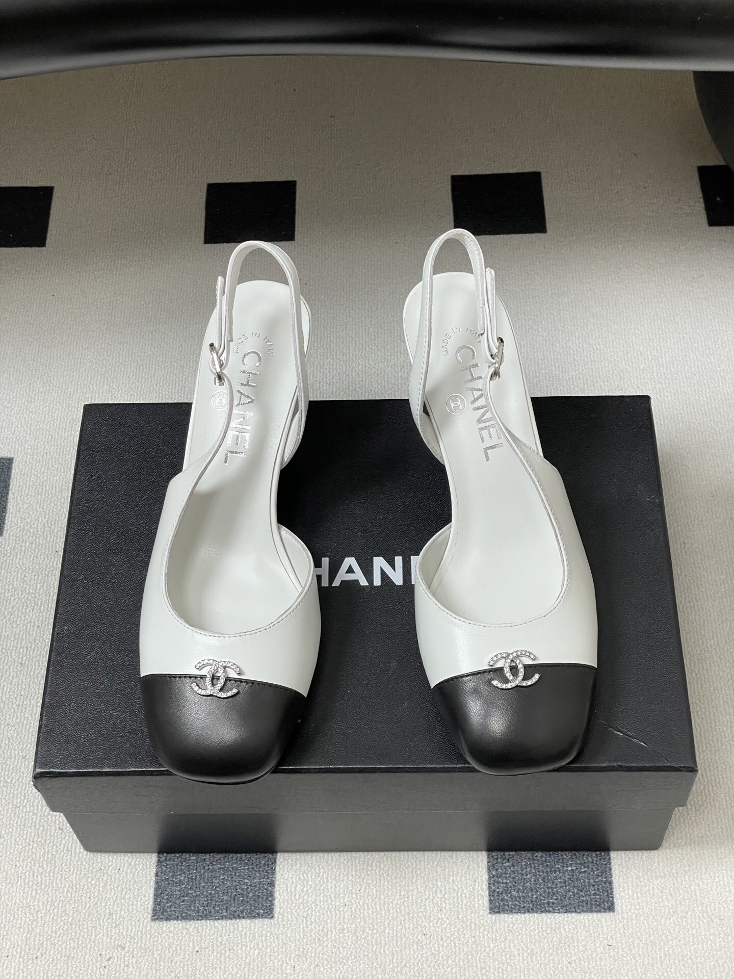 Pair of Chanel white leather slingback pumps with black toe caps and crystal CC logos on a black table. - Hình 5