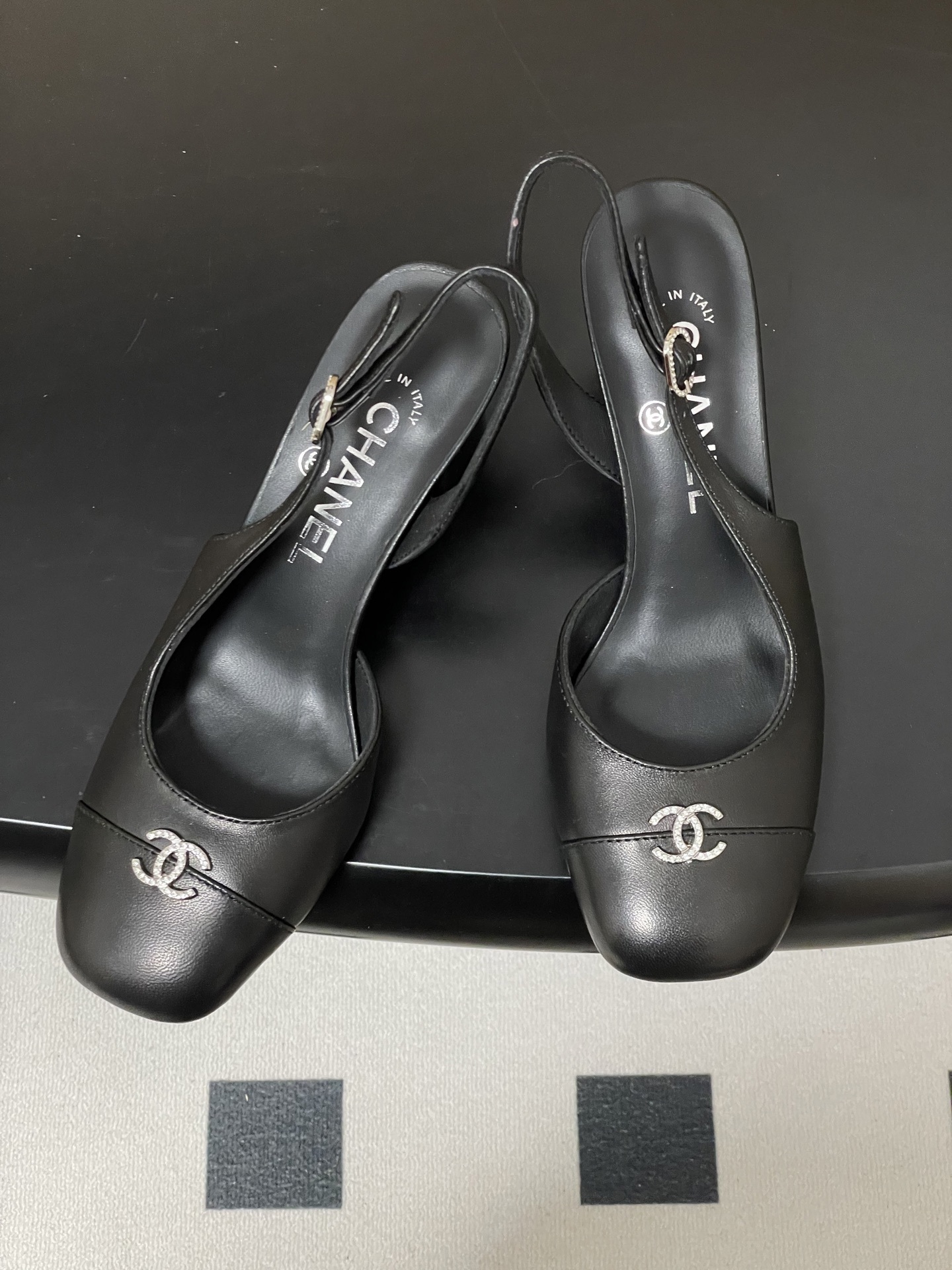 A pair of luxury black leather Chanel slingback pumps with crystal CC logos on the toes and block heels. - Hình 2