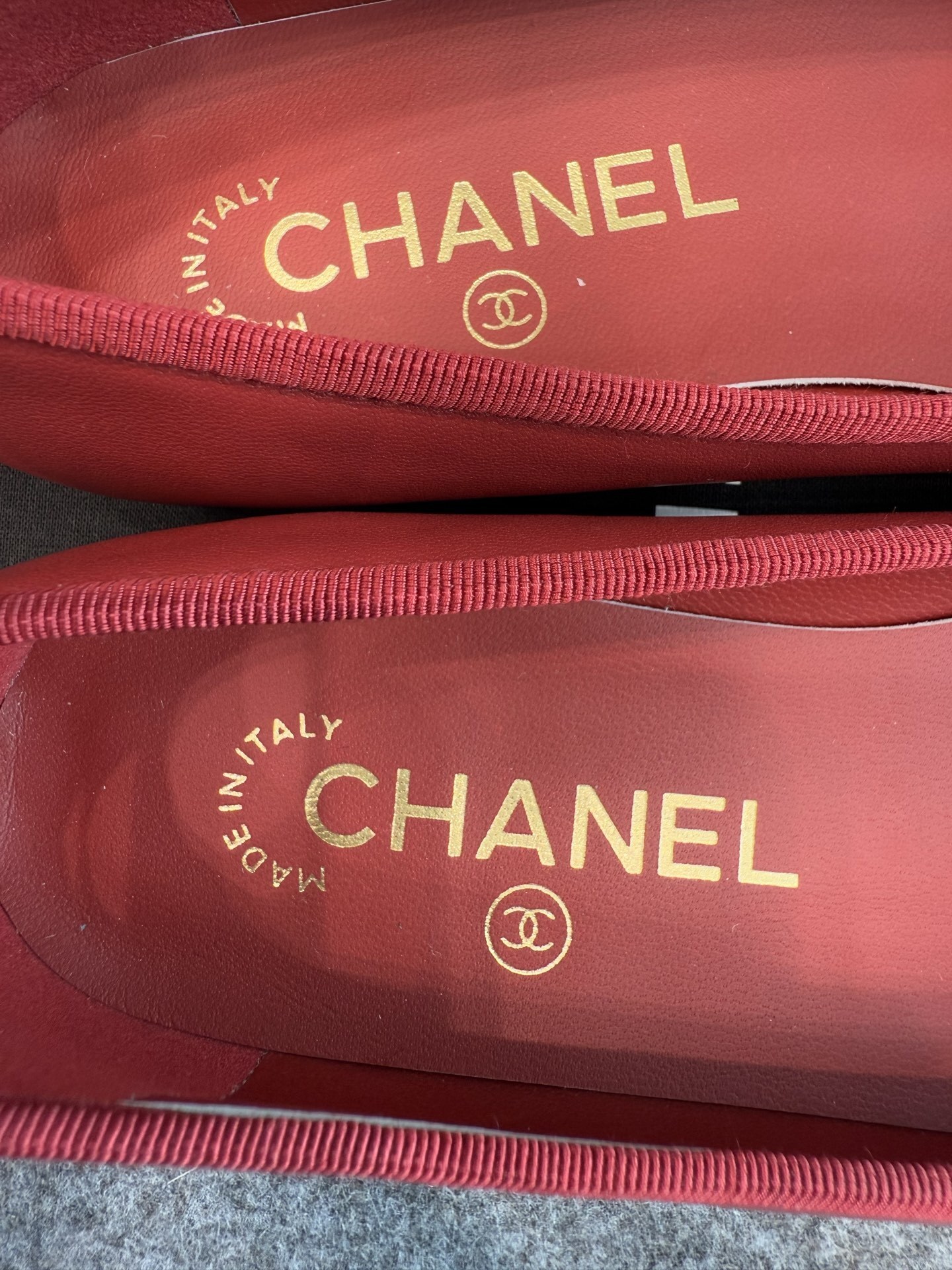A pair of red Chanel ballet flats with black leather toe caps featuring the CC logo and a small bow, displayed with original packaging. - Hình 11