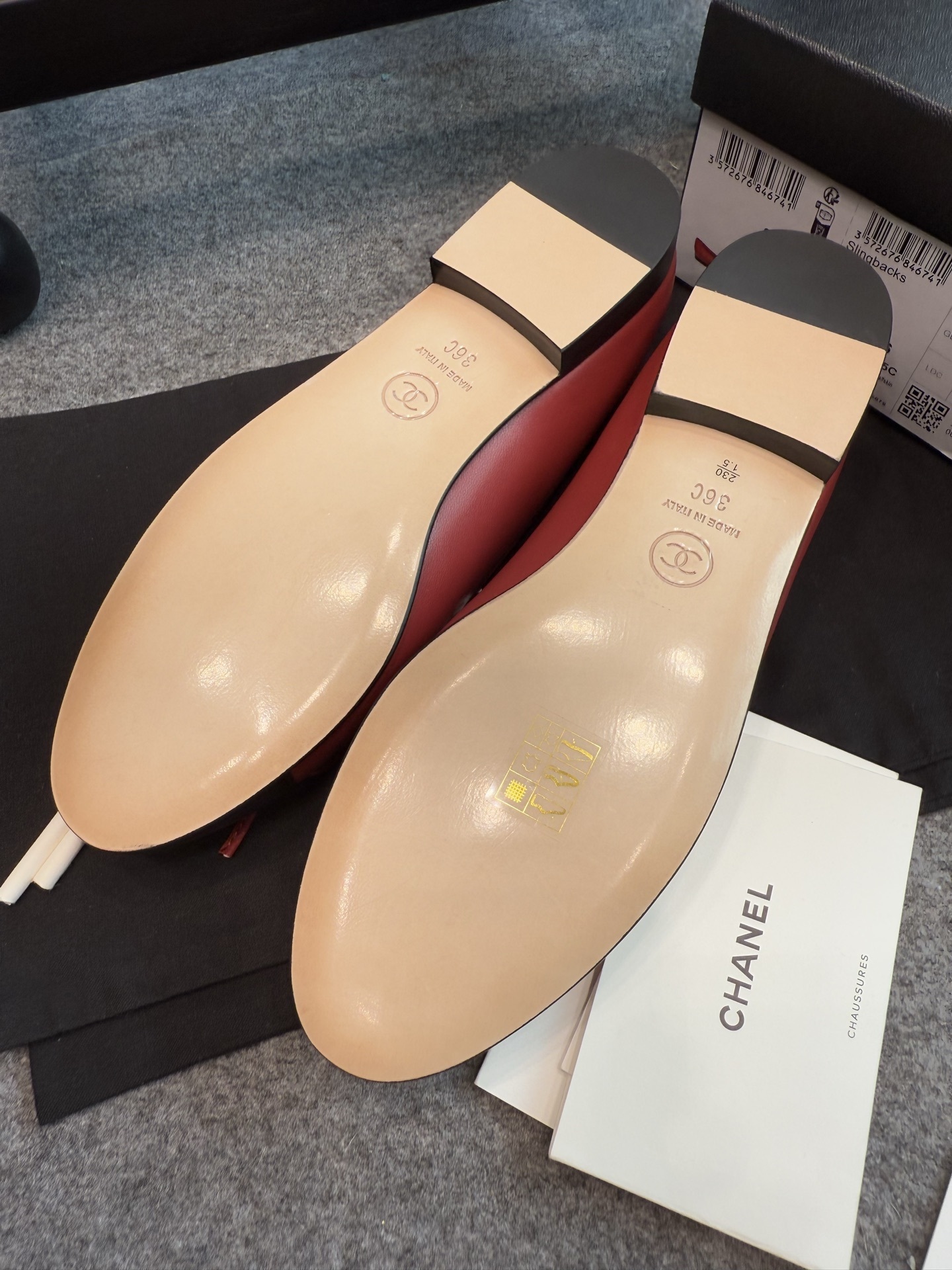 A pair of red Chanel ballet flats with black leather toe caps featuring the CC logo and a small bow, displayed with original packaging. - Hình 10