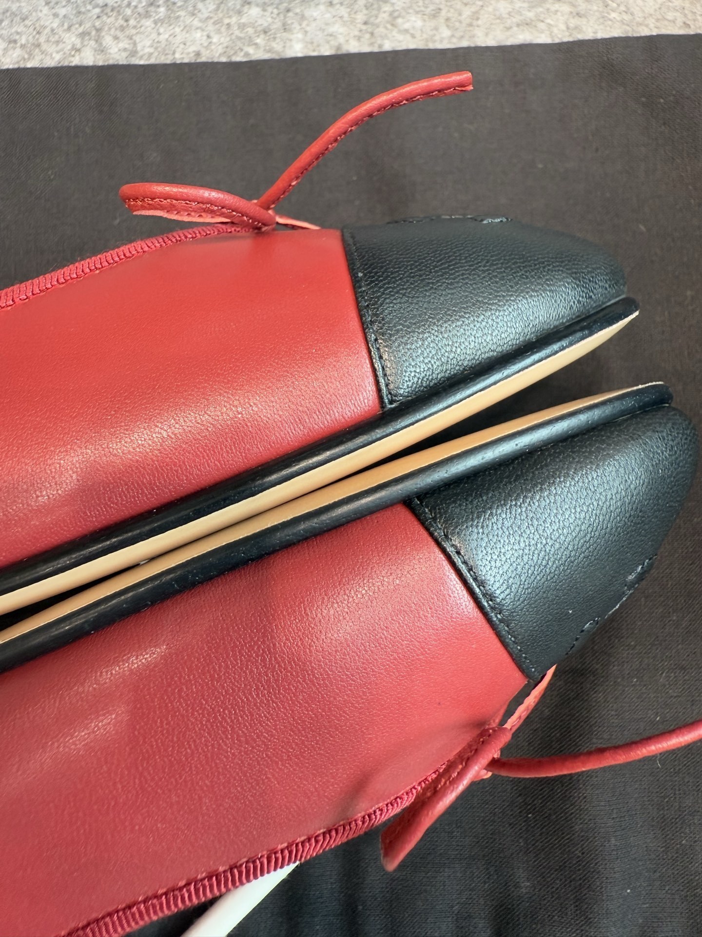 A pair of red Chanel ballet flats with black leather toe caps featuring the CC logo and a small bow, displayed with original packaging. - Hình 7