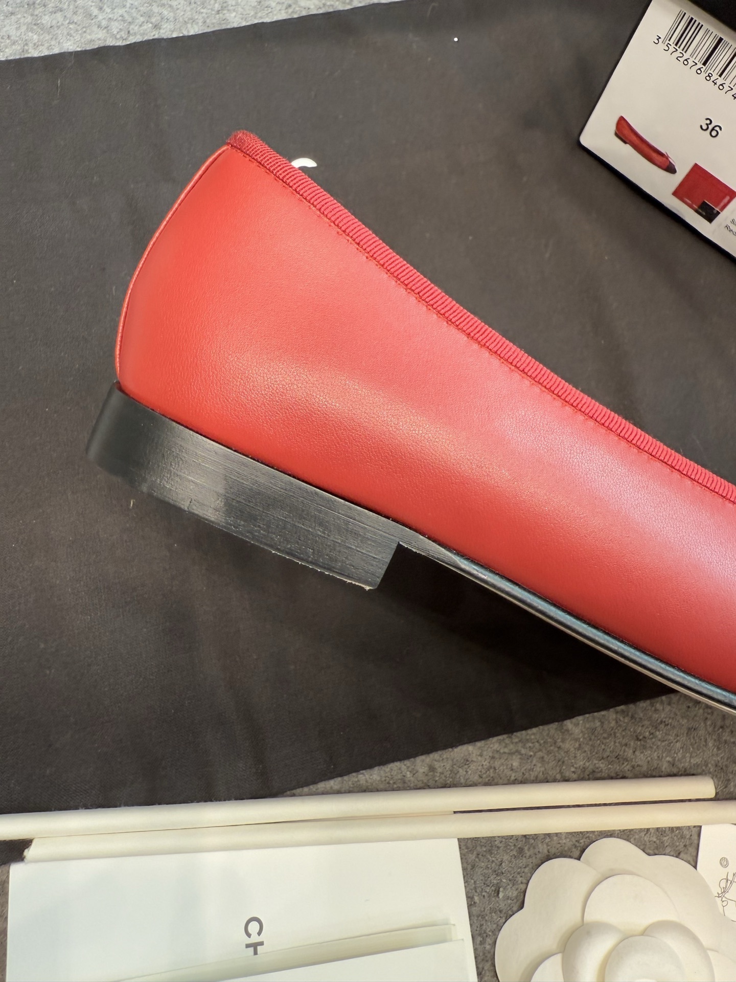 A pair of red Chanel ballet flats with black leather toe caps featuring the CC logo and a small bow, displayed with original packaging. - Hình 5