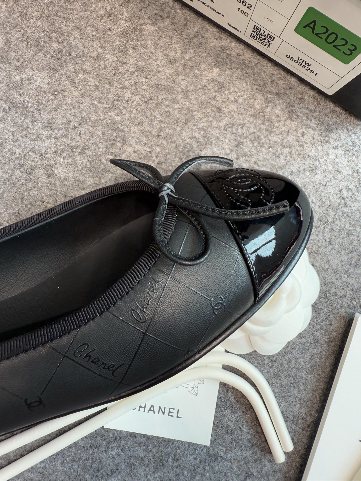 A pair of black Chanel quilted lambskin ballerina flats with patent leather CC toe caps and front bows, displayed with original luxury packaging. - Hình 6