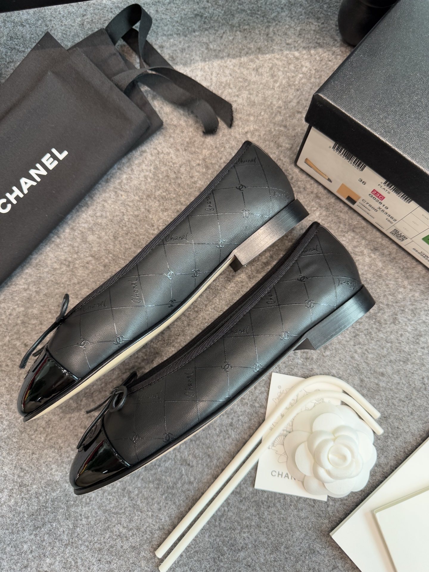 A pair of black Chanel quilted lambskin ballerina flats with patent leather CC toe caps and front bows, displayed with original luxury packaging. - Hình 5