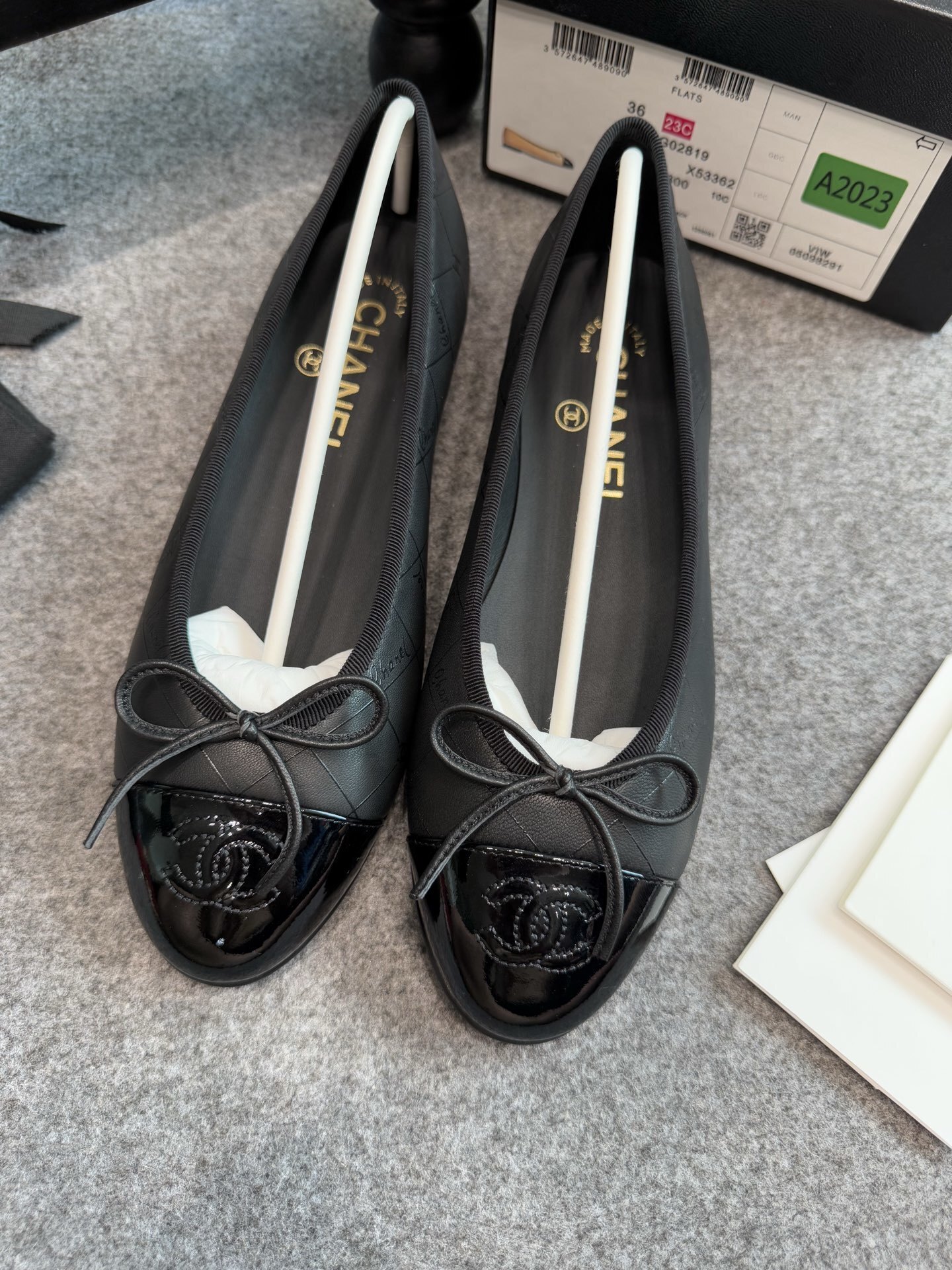 A pair of black Chanel quilted lambskin ballerina flats with patent leather CC toe caps and front bows, displayed with original luxury packaging. - Hình 4