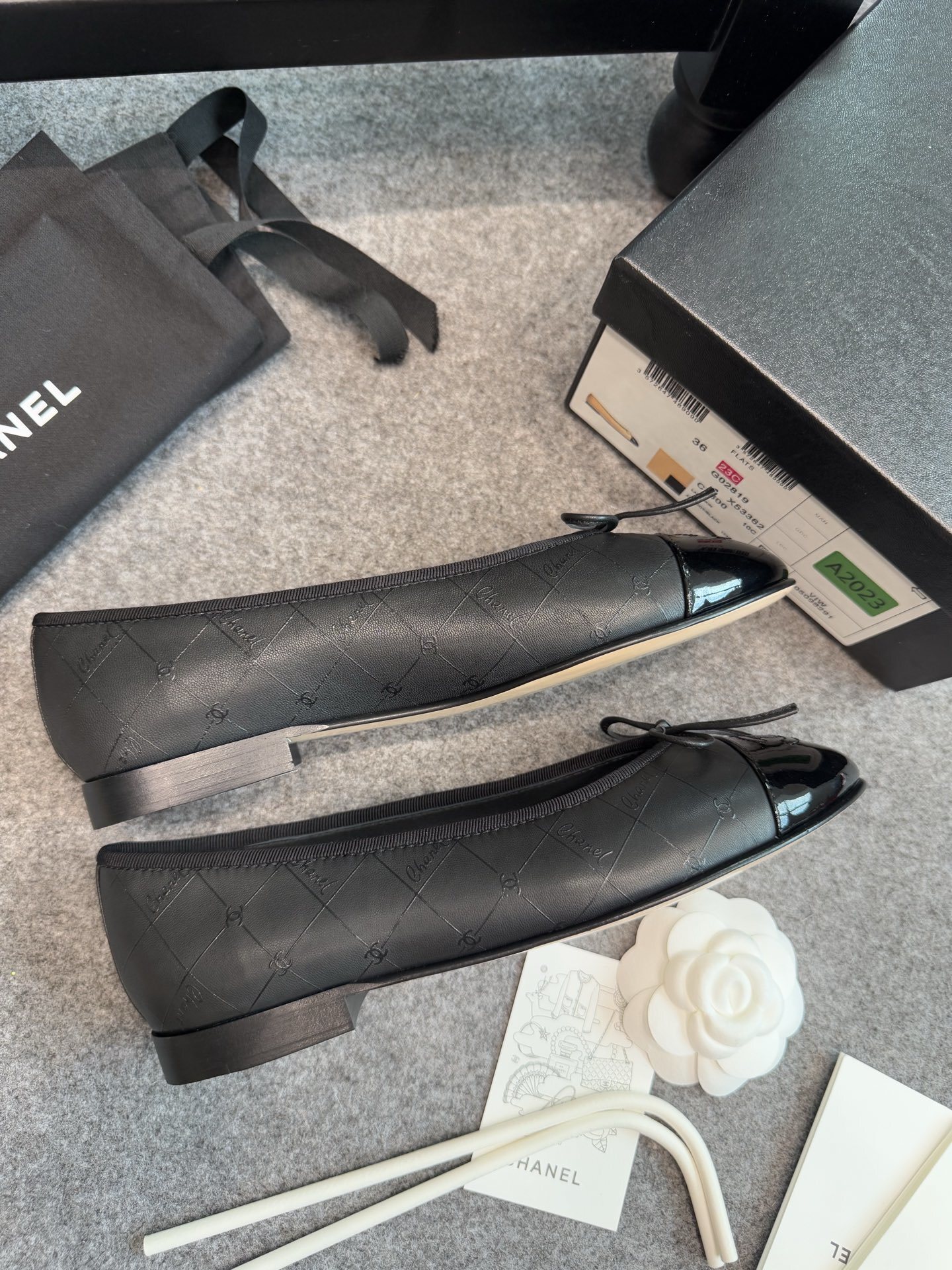 A pair of black Chanel quilted lambskin ballerina flats with patent leather CC toe caps and front bows, displayed with original luxury packaging. - Hình 3