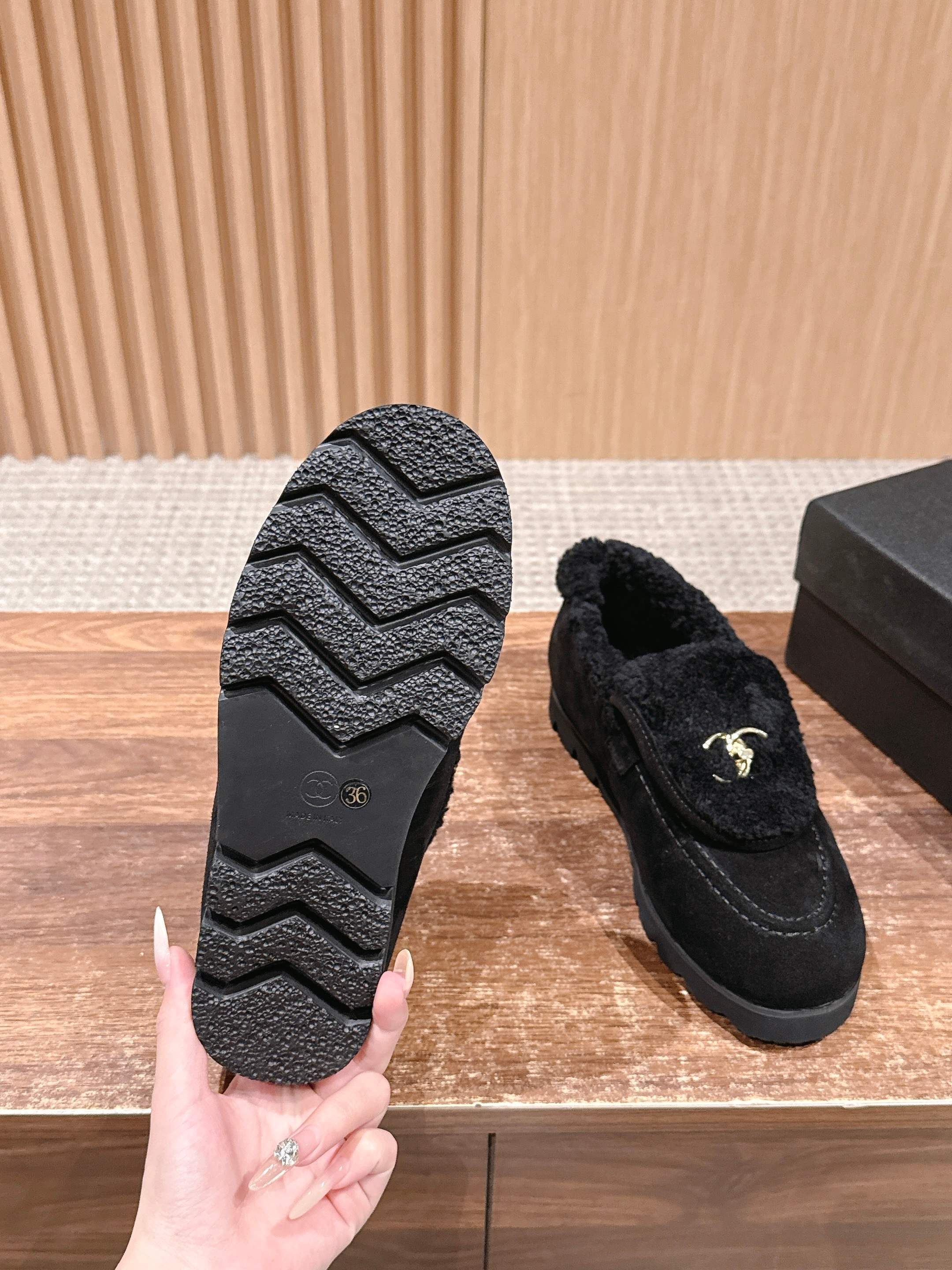 Pair of black suede loafers with thick shearling lining and a gold interlocking logo on the front sitting on a wooden surface. - Hình 9