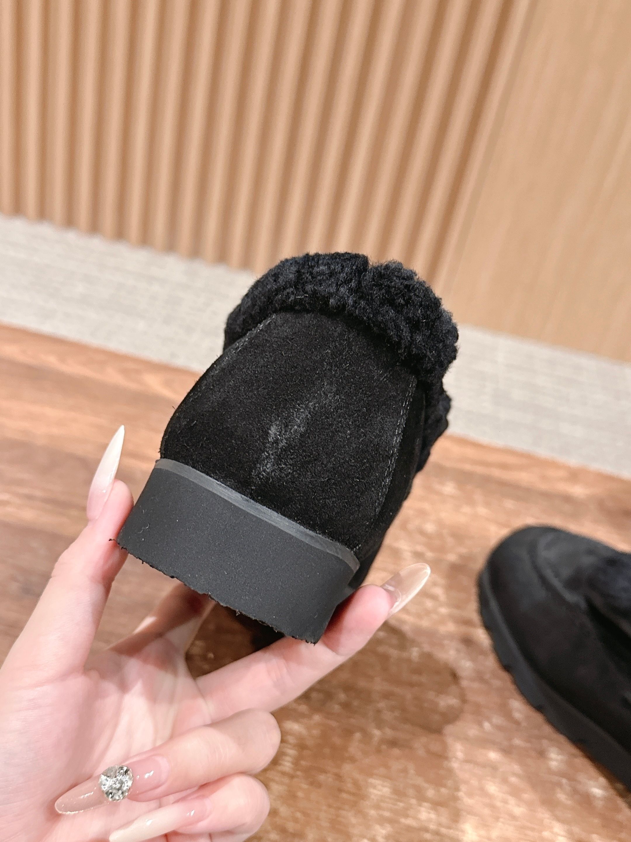 Pair of black suede loafers with thick shearling lining and a gold interlocking logo on the front sitting on a wooden surface. - Hình 8