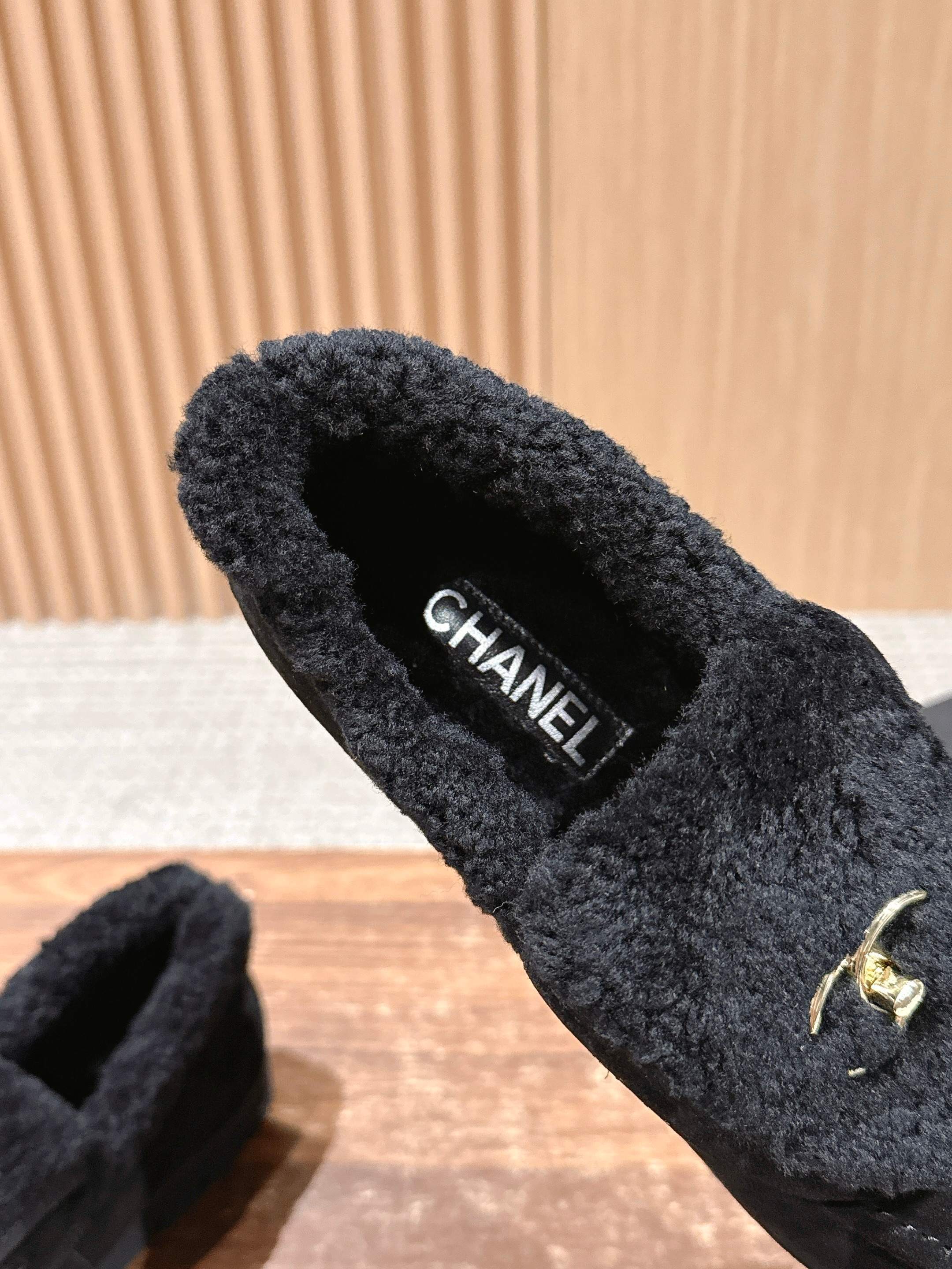 Pair of black suede loafers with thick shearling lining and a gold interlocking logo on the front sitting on a wooden surface. - Hình 6