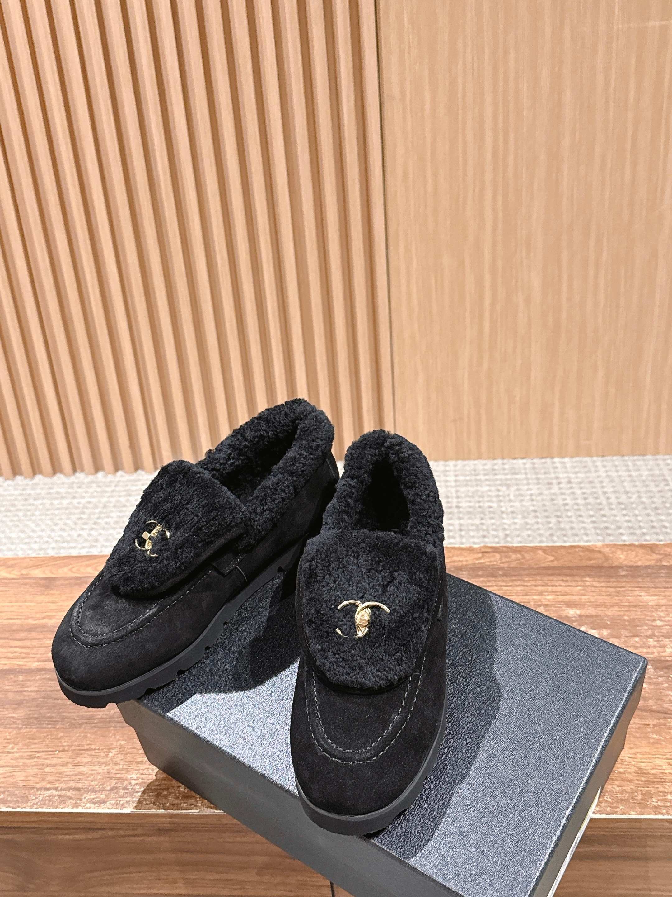 Pair of black suede loafers with thick shearling lining and a gold interlocking logo on the front sitting on a wooden surface. - Hình 4