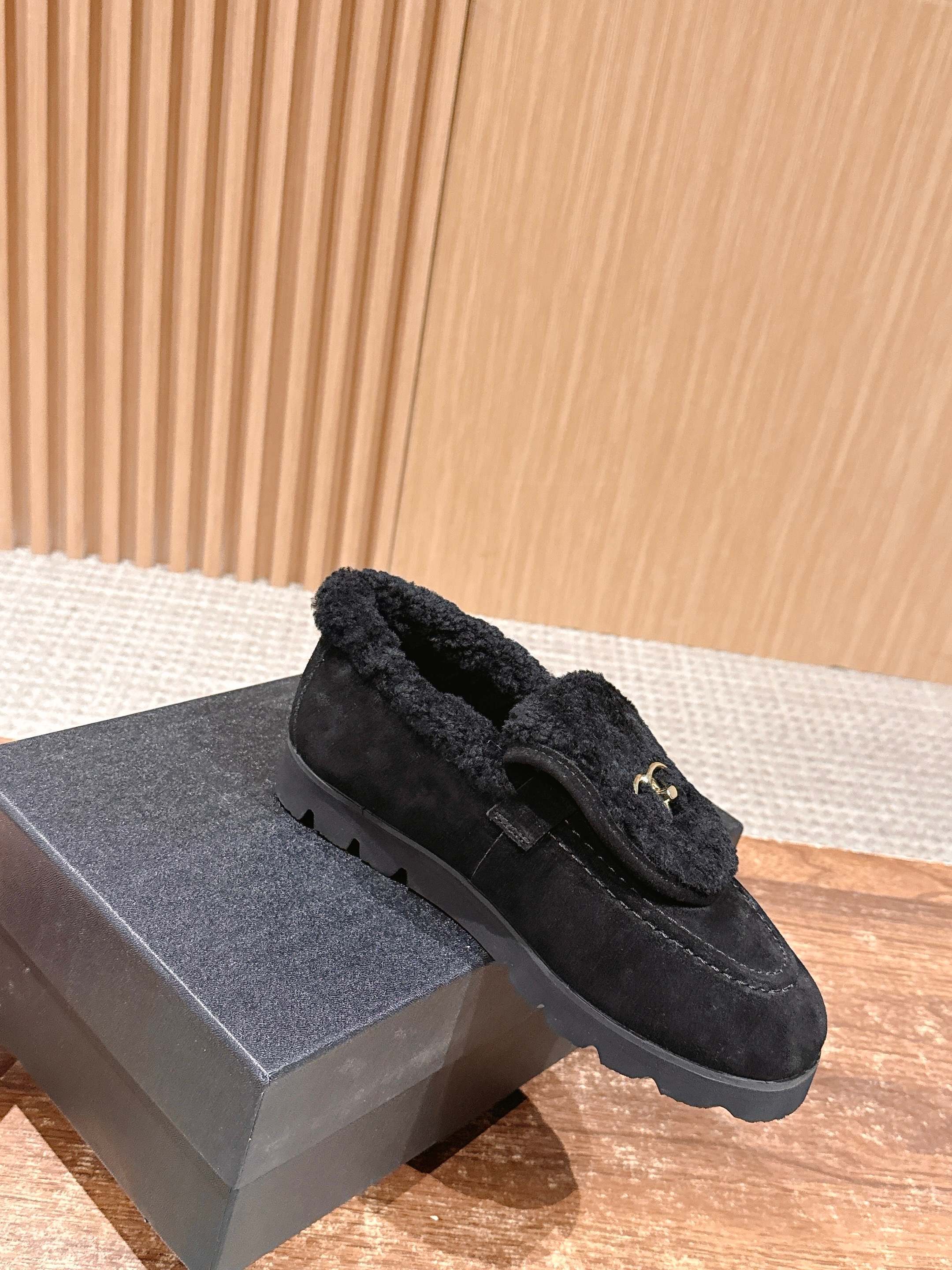 Pair of black suede loafers with thick shearling lining and a gold interlocking logo on the front sitting on a wooden surface. - Hình 3