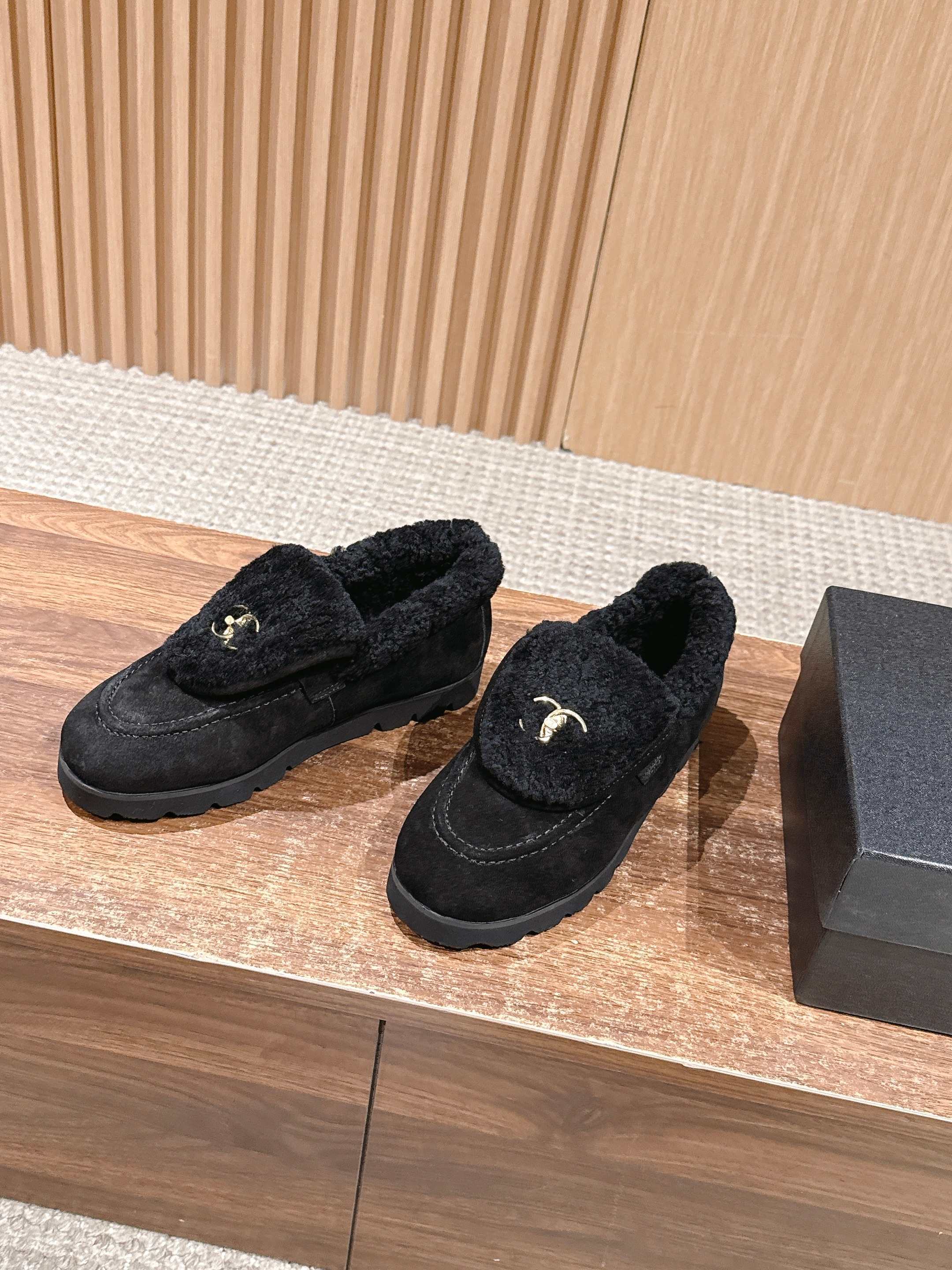 Pair of black suede loafers with thick shearling lining and a gold interlocking logo on the front sitting on a wooden surface. - Hình 2