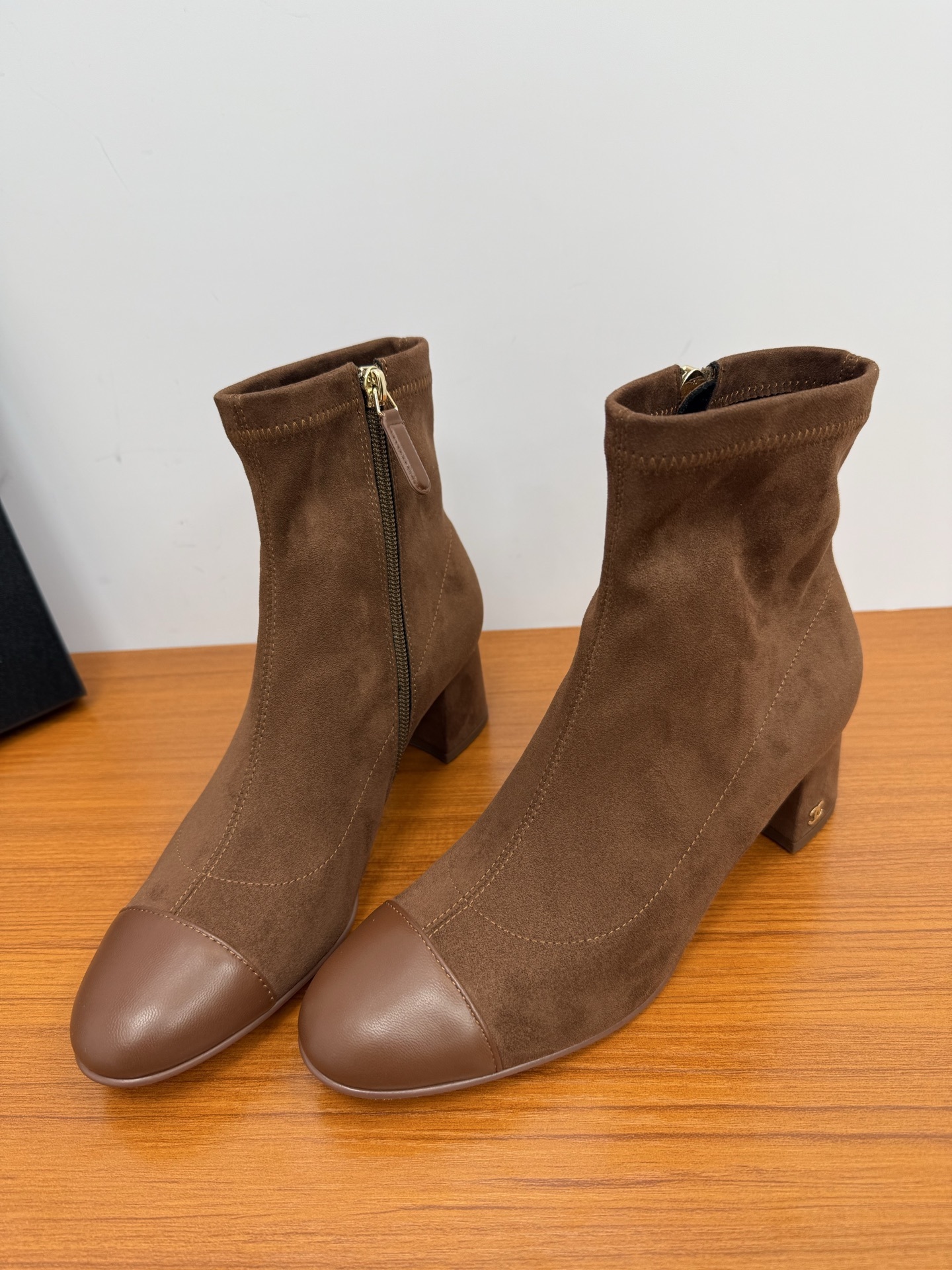 Pair of brown suede ankle boots with smooth leather toe caps and gold side zippers on a wooden surface. - Hình 5