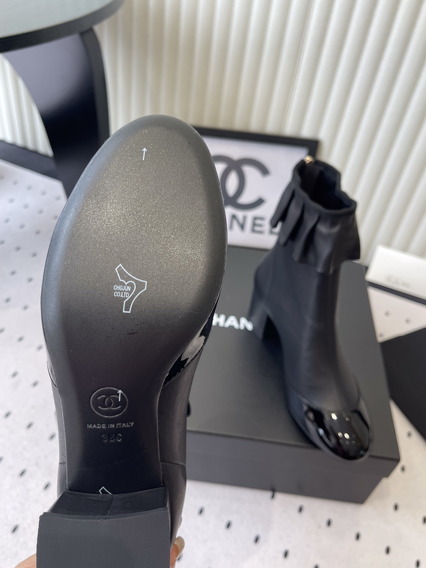 Luxury black leather ankle boots featuring a ruffle cuff detail and shiny patent leather cap toe on a designer box. - Hình 9