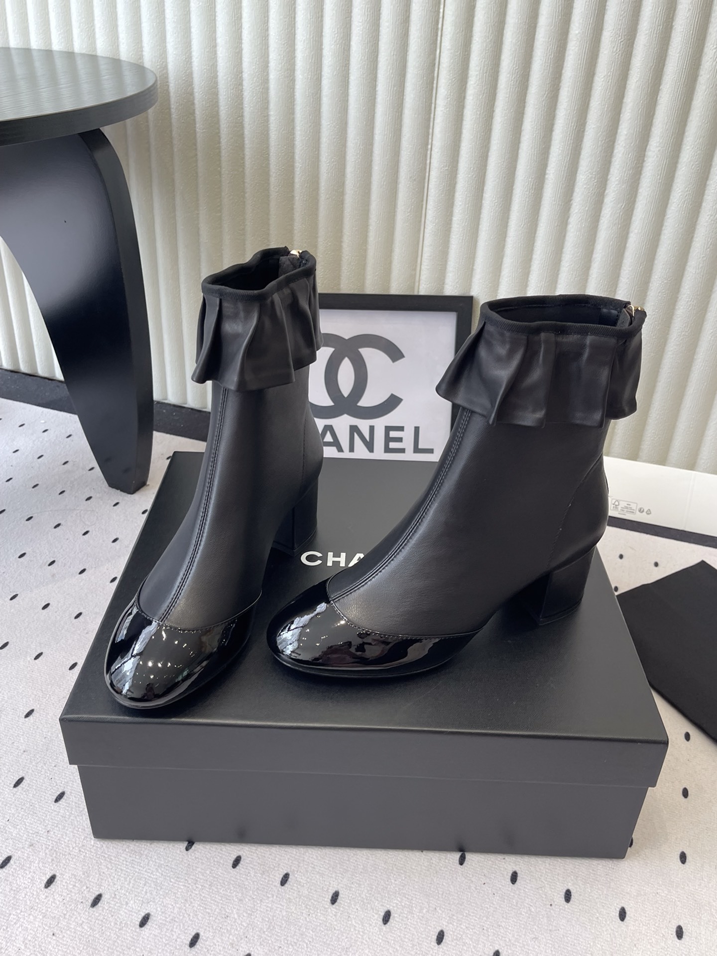 Luxury black leather ankle boots featuring a ruffle cuff detail and shiny patent leather cap toe on a designer box. - Hình 8