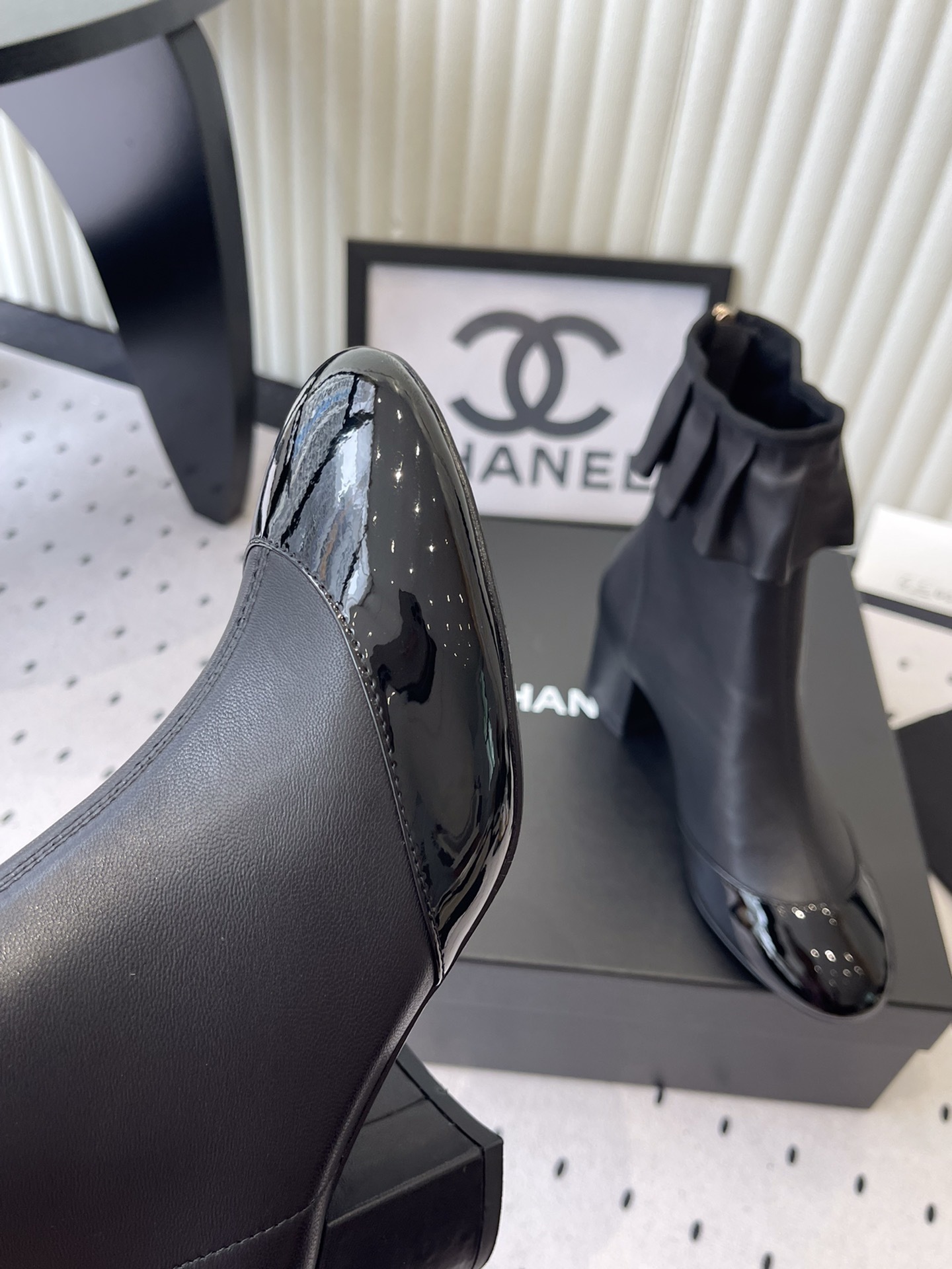 Luxury black leather ankle boots featuring a ruffle cuff detail and shiny patent leather cap toe on a designer box. - Hình 6