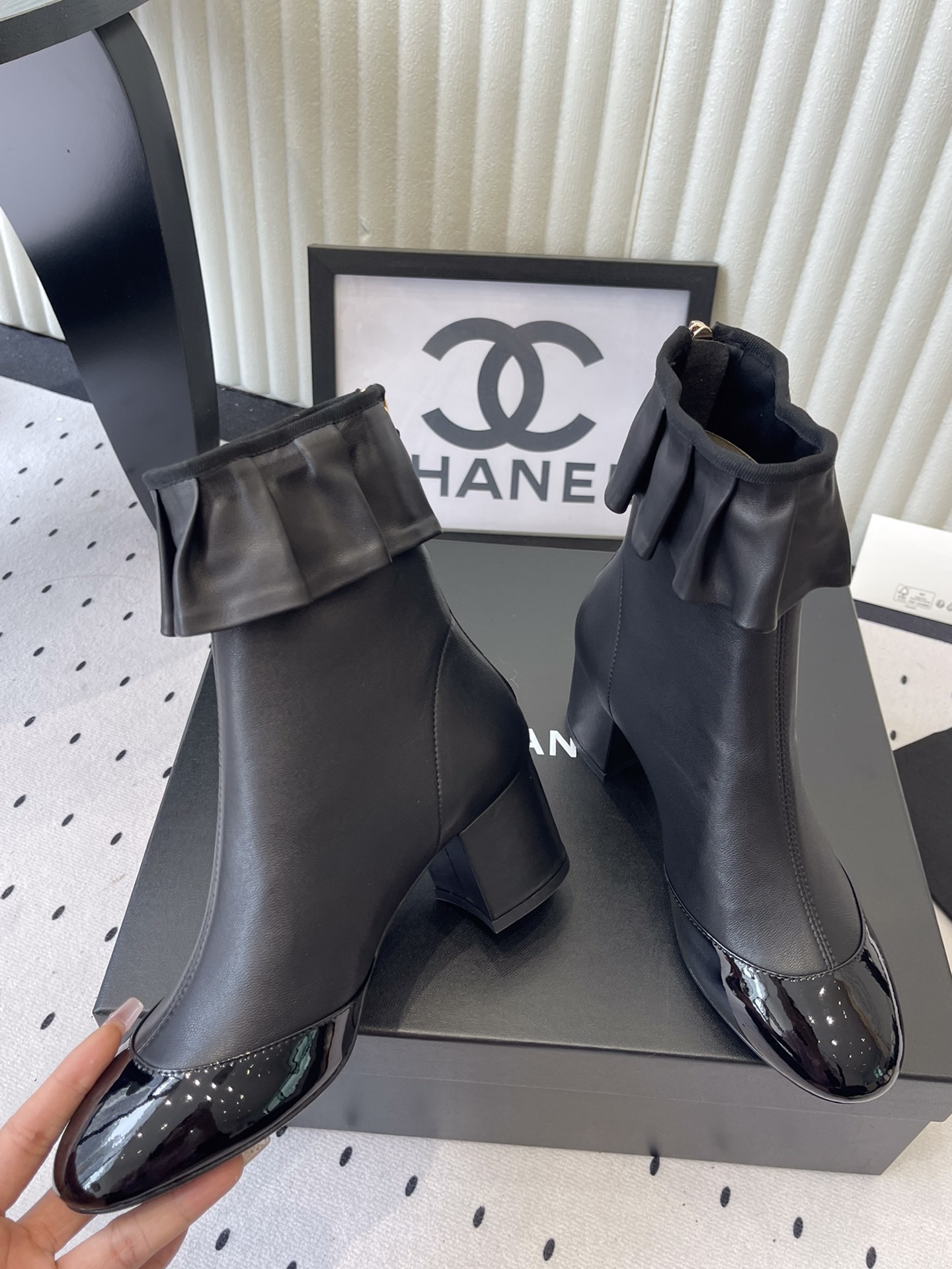 Luxury black leather ankle boots featuring a ruffle cuff detail and shiny patent leather cap toe on a designer box. - Hình 5