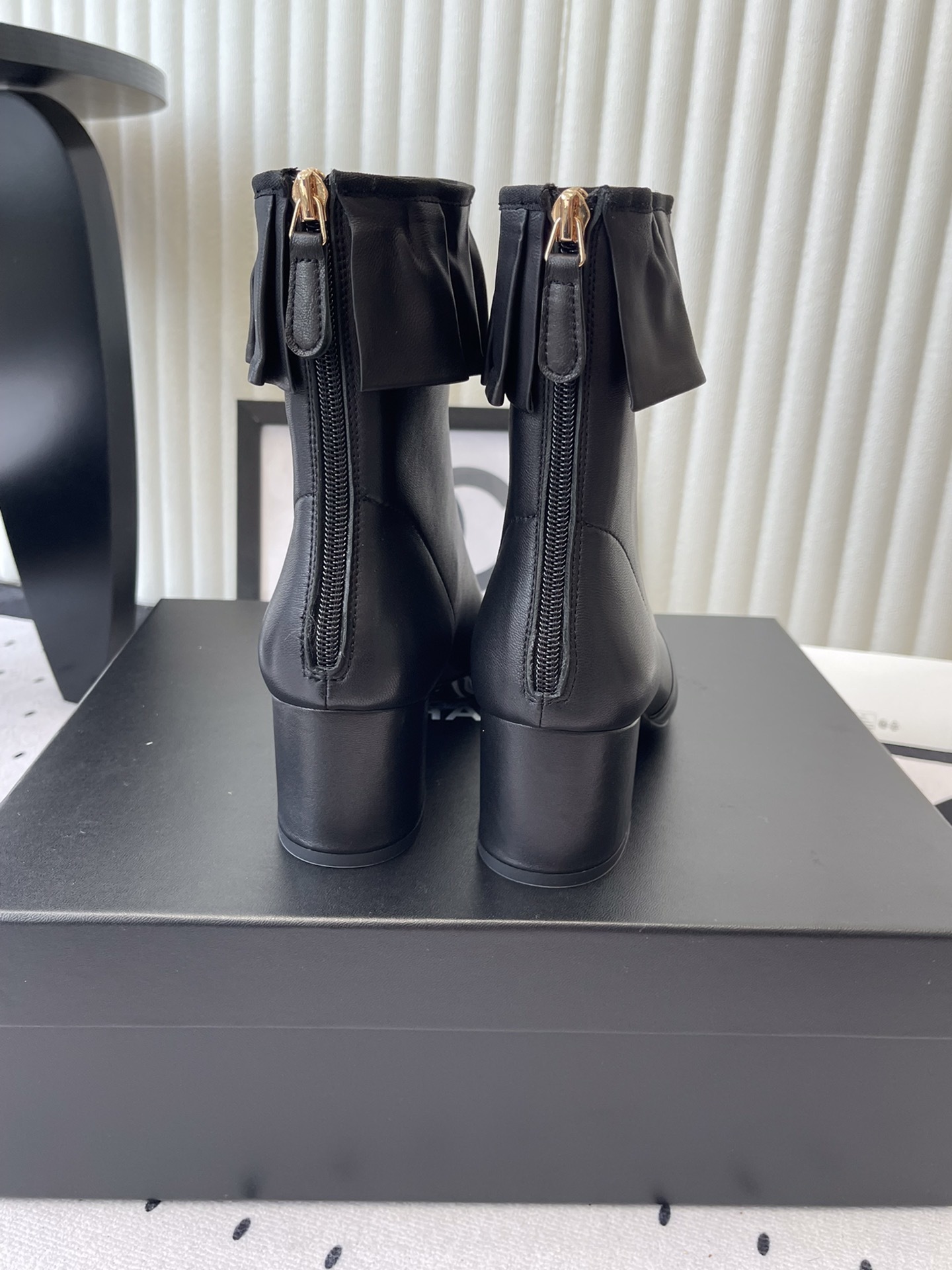 Luxury black leather ankle boots featuring a ruffle cuff detail and shiny patent leather cap toe on a designer box. - Hình 3