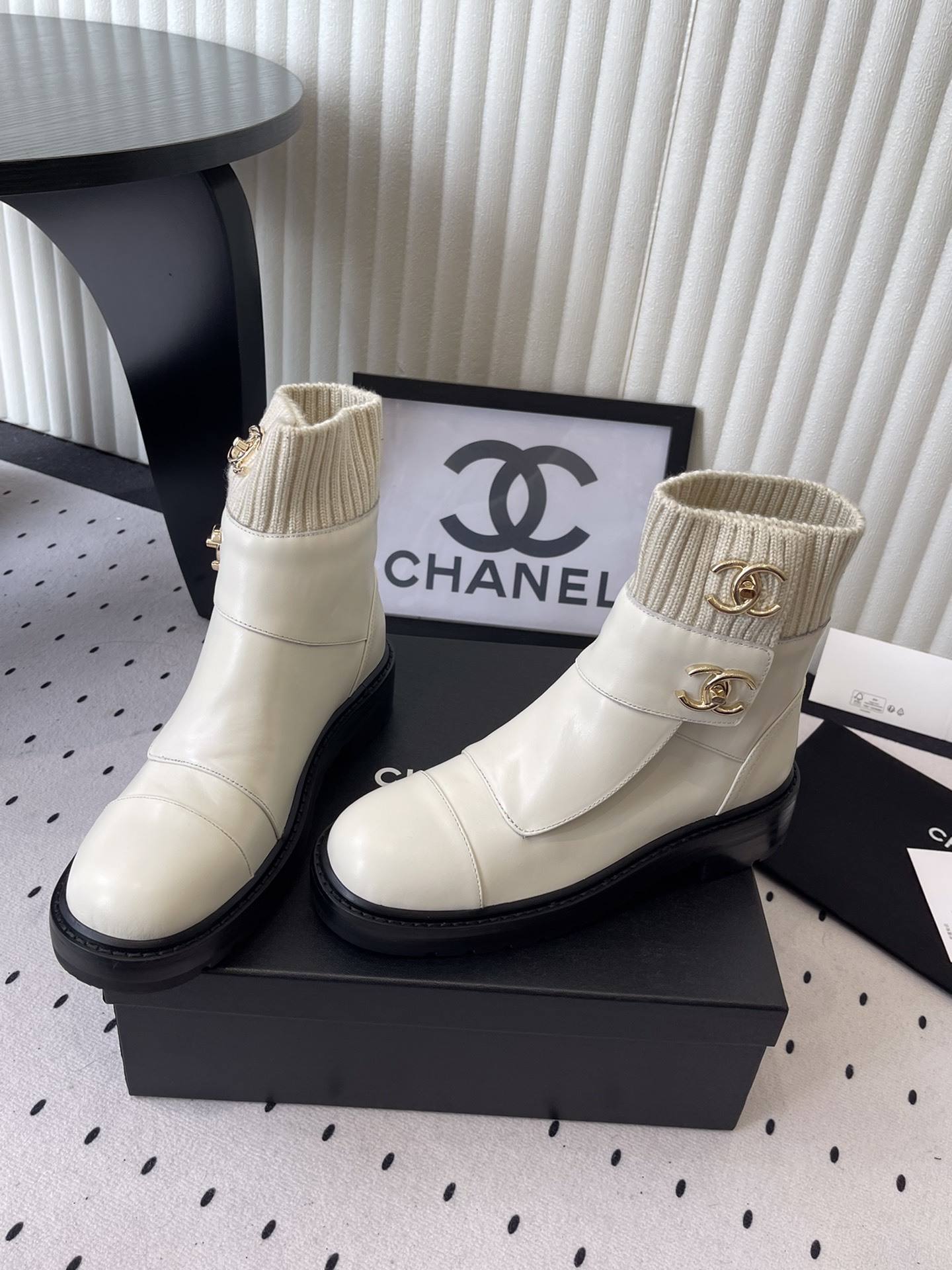 Pair of Chanel off-white leather ankle boots with ribbed knit collars and gold CC logos displayed on a black box. - Hình 8