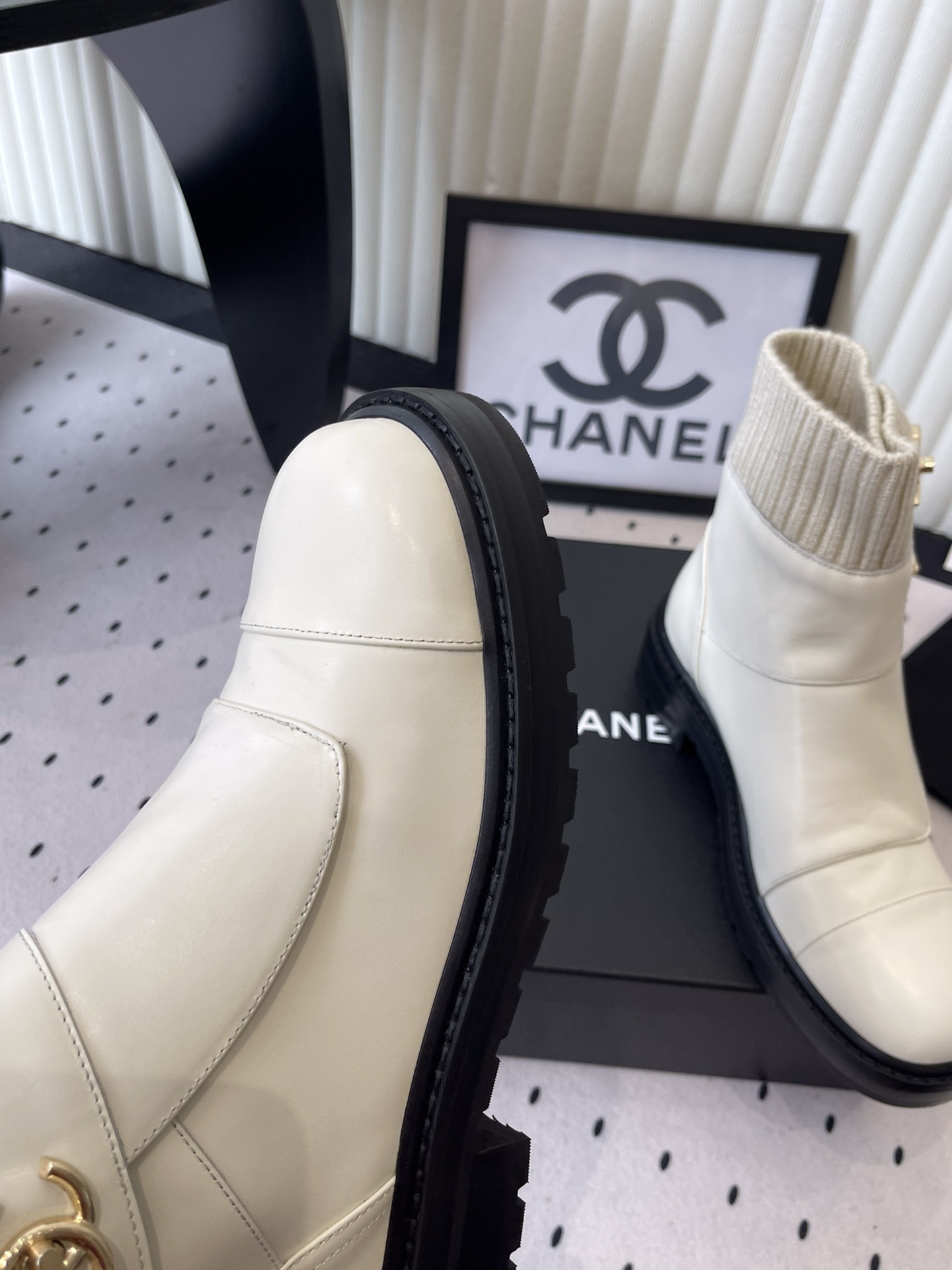 Pair of Chanel off-white leather ankle boots with ribbed knit collars and gold CC logos displayed on a black box. - Hình 6