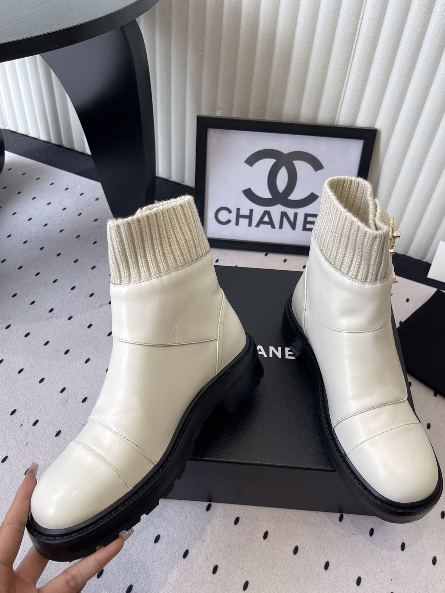 Pair of Chanel off-white leather ankle boots with ribbed knit collars and gold CC logos displayed on a black box. - Hình 5