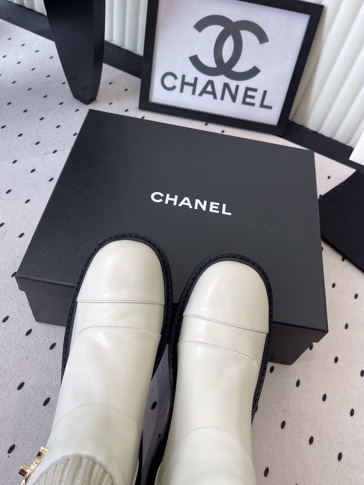 Pair of Chanel off-white leather ankle boots with ribbed knit collars and gold CC logos displayed on a black box. - Hình 4