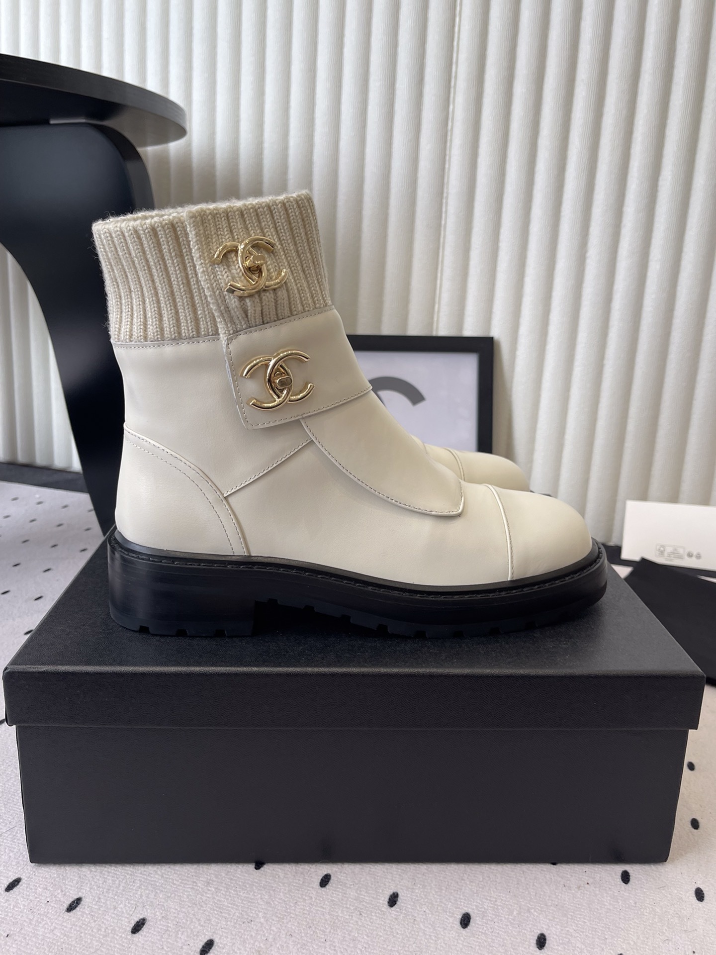 Pair of Chanel off-white leather ankle boots with ribbed knit collars and gold CC logos displayed on a black box. - Hình 2