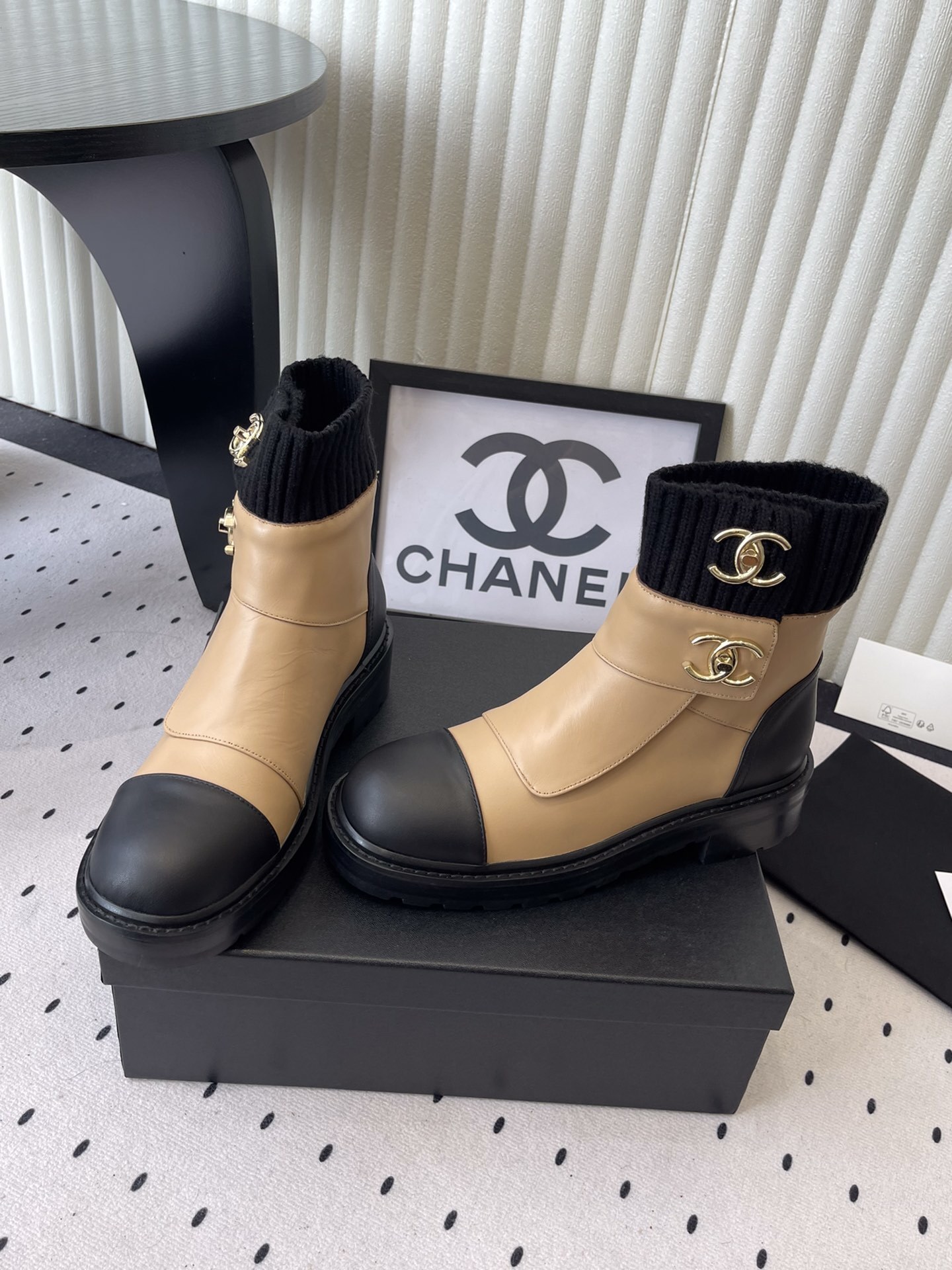 Pair of Chanel beige and black leather ankle boots with gold CC logo and black knit sock collar displayed on a black box. - Hình 8