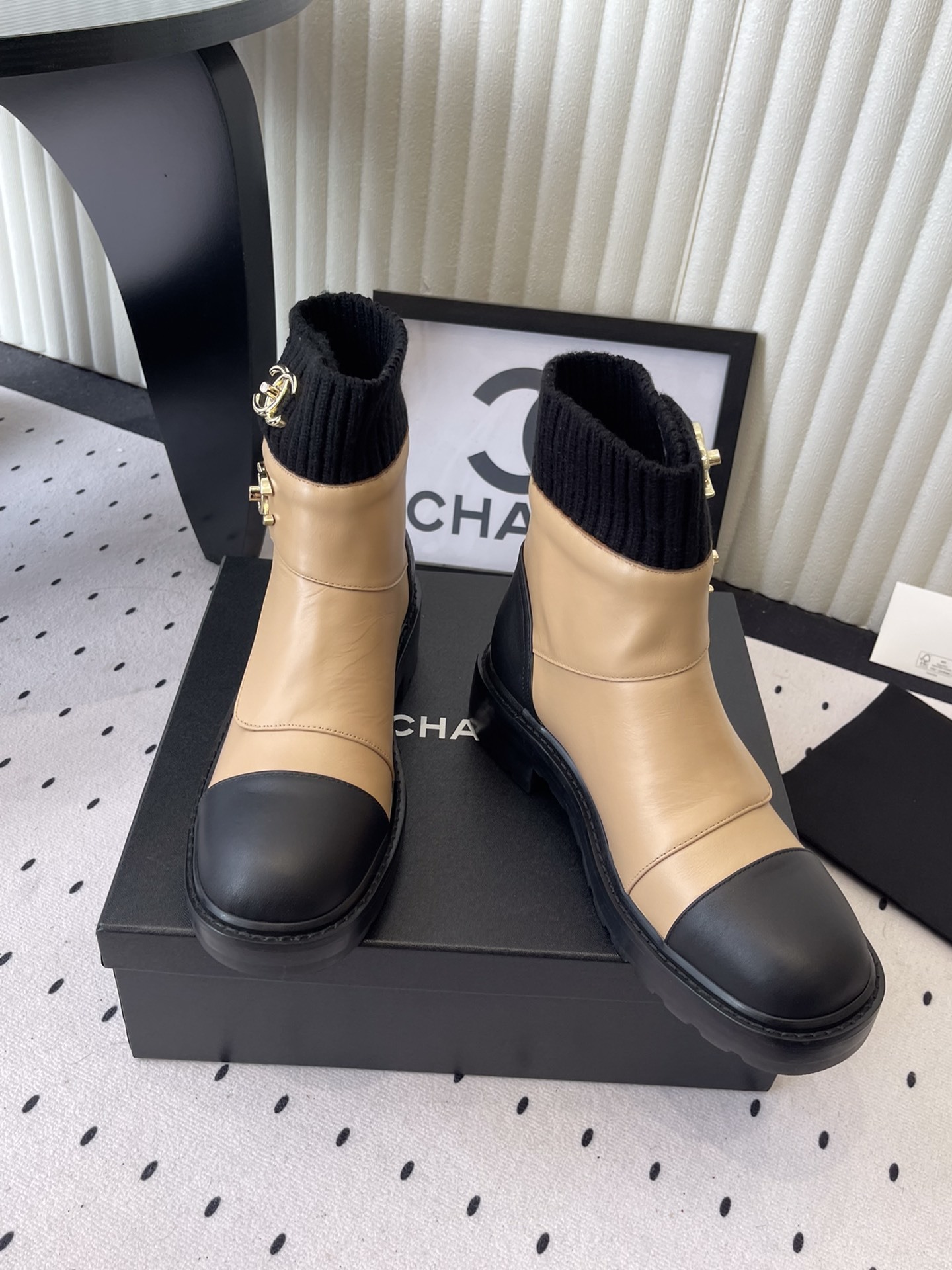 Pair of Chanel beige and black leather ankle boots with gold CC logo and black knit sock collar displayed on a black box. - Hình 7