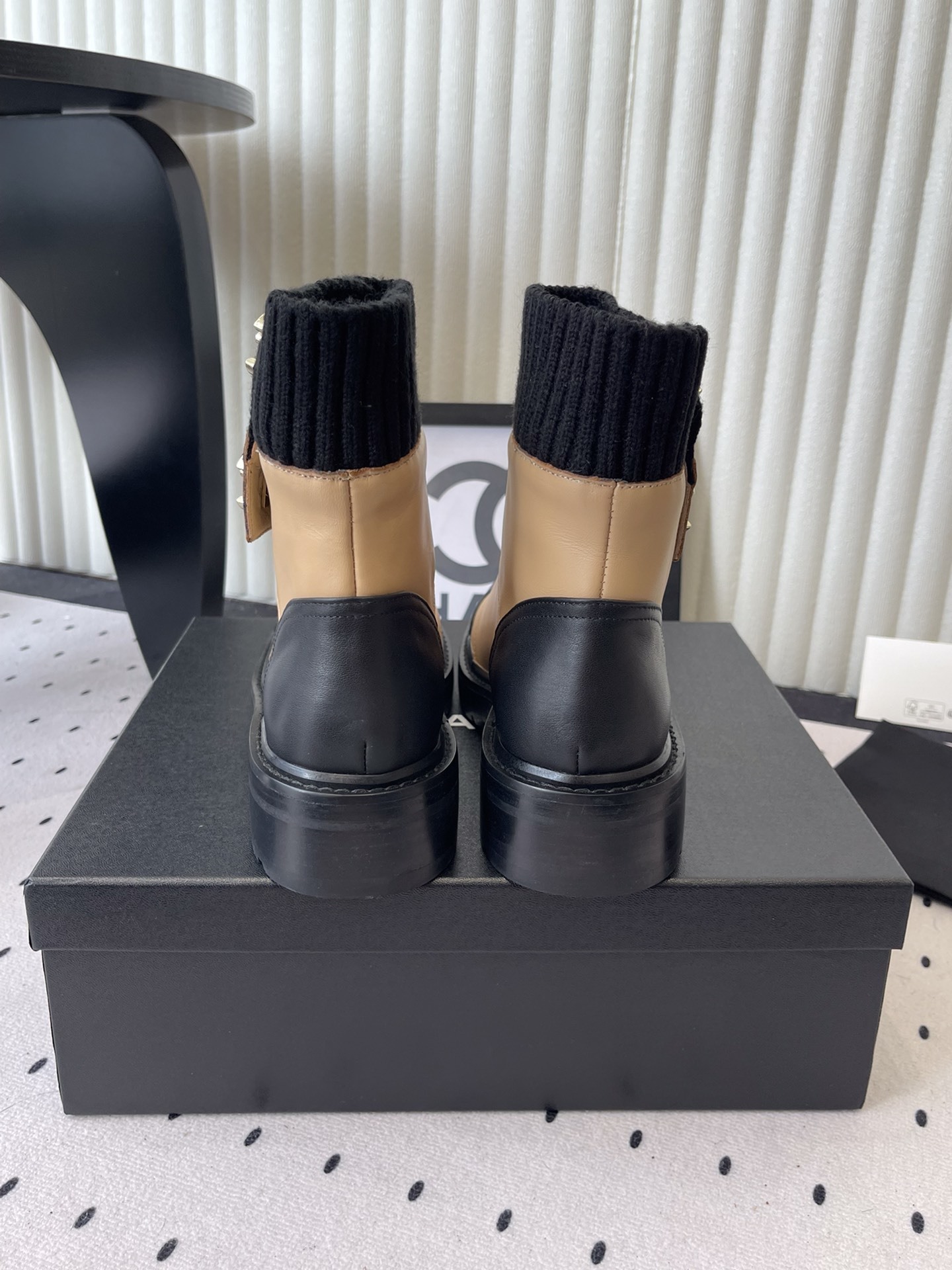 Pair of Chanel beige and black leather ankle boots with gold CC logo and black knit sock collar displayed on a black box. - Hình 3